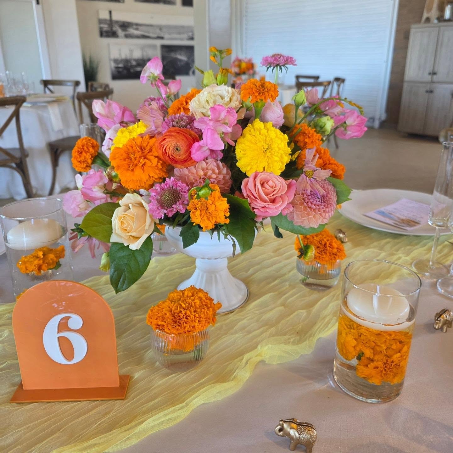 Colorful flower arrangement with pink, yellow, orange, and purple flowers in a white vase on a table, with table number 6.