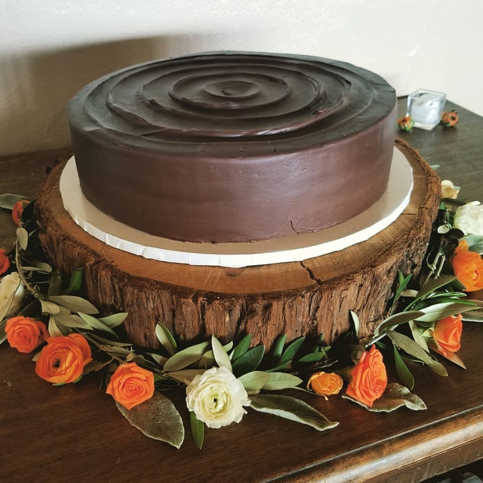 Chocolate cake on a wooden log base, decorated with orange and white flowers, with a white border around the cake.