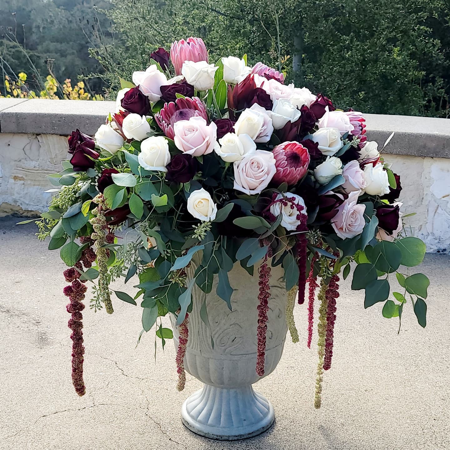 Large floral arrangement with white, pink, and dark purple flowers in a white vase outdoors.