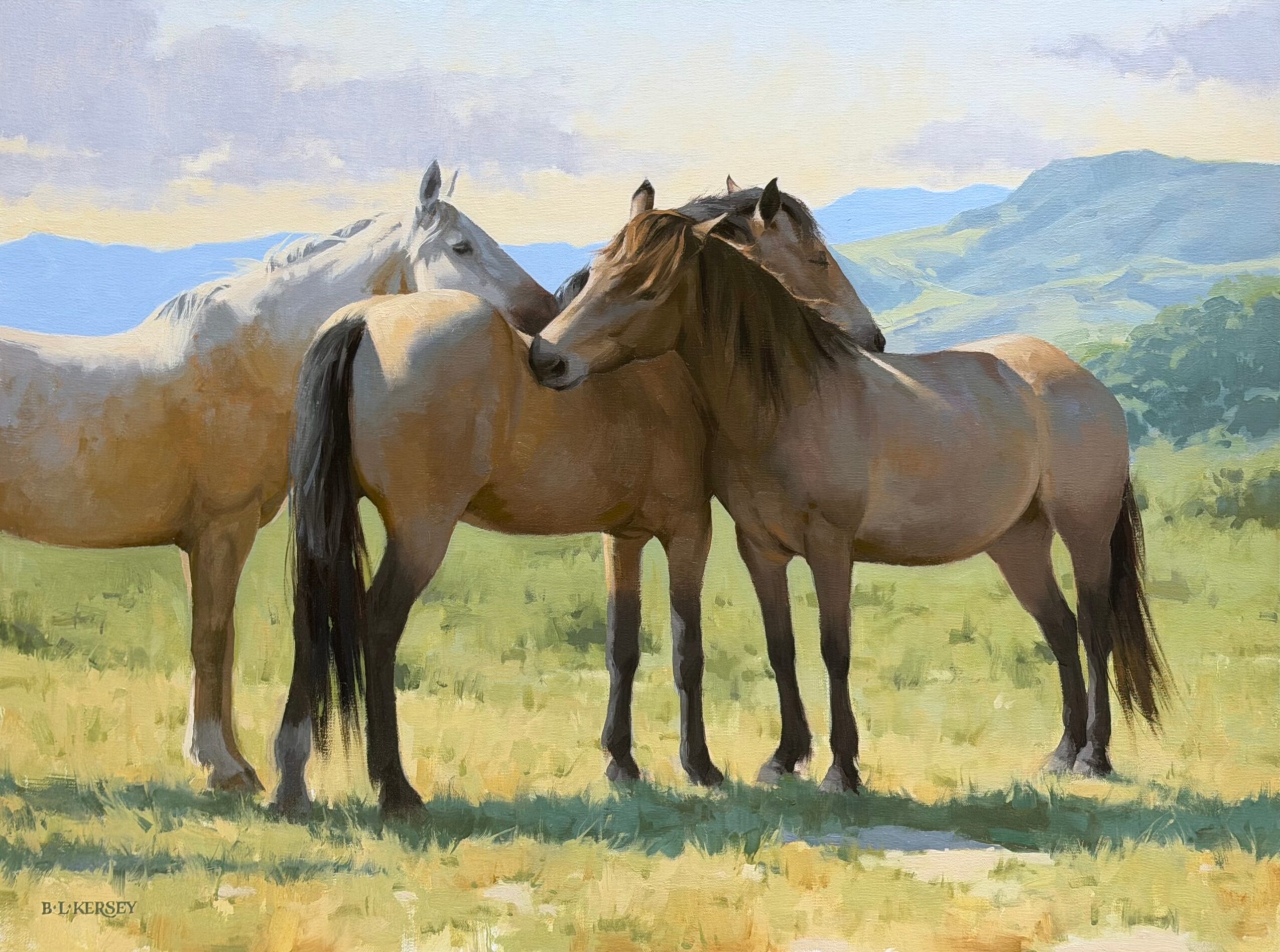 Three horses standing in a grassy field with mountains in the background, two touching heads, one facing away.