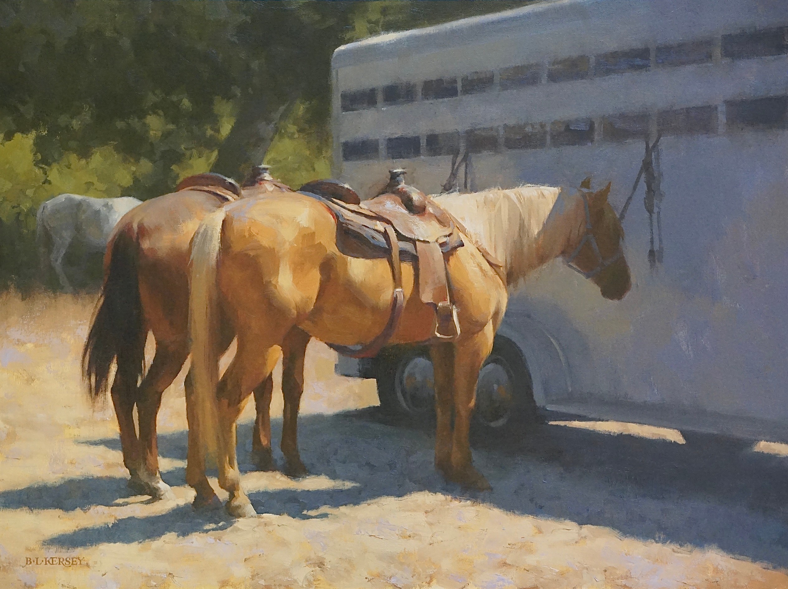 Two horses with saddles stand near a trailer and a vehicle outdoors, with trees in the background.