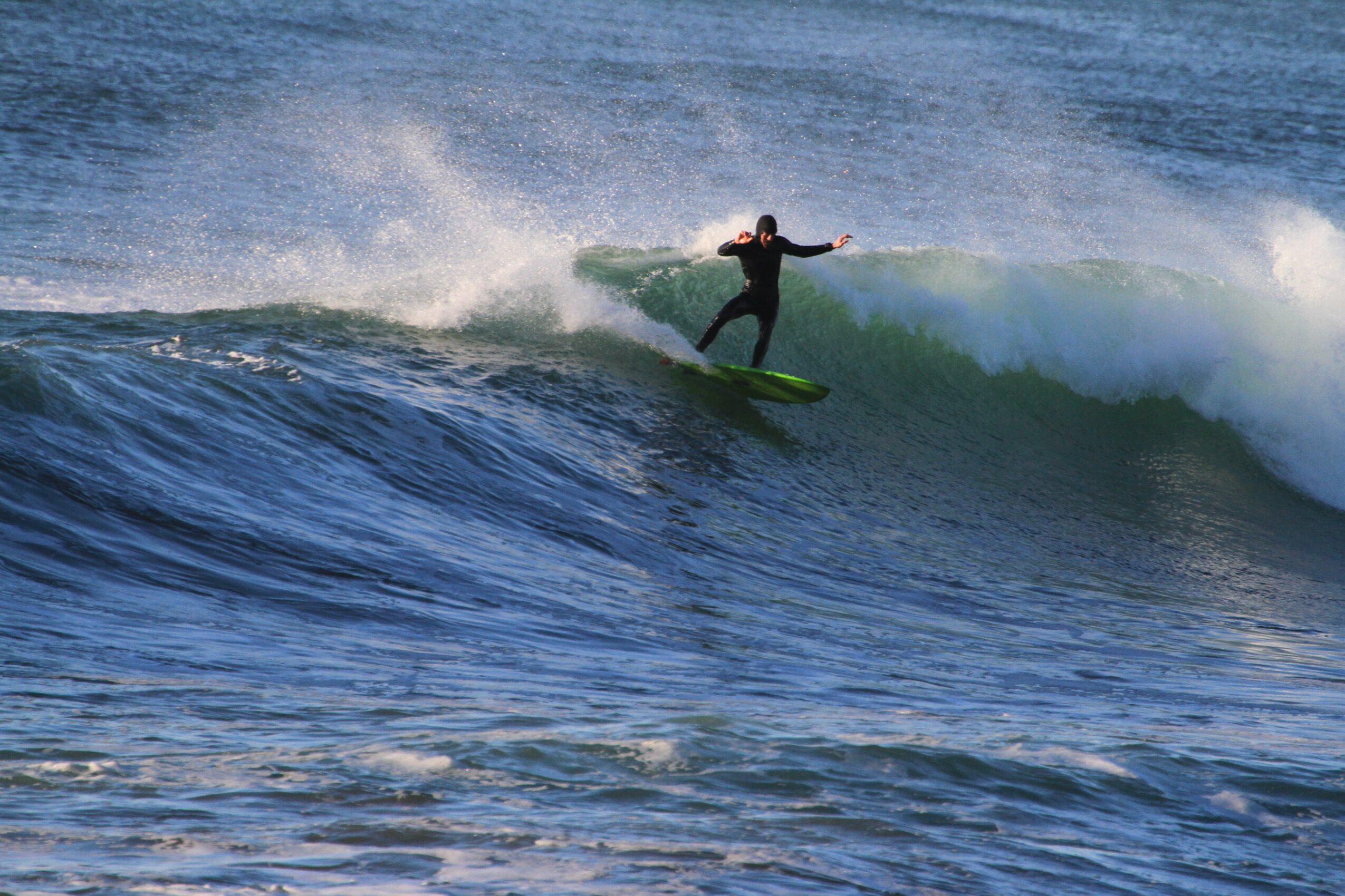 Person surfing on a wave with water spray, arms outstretched, in ocean water