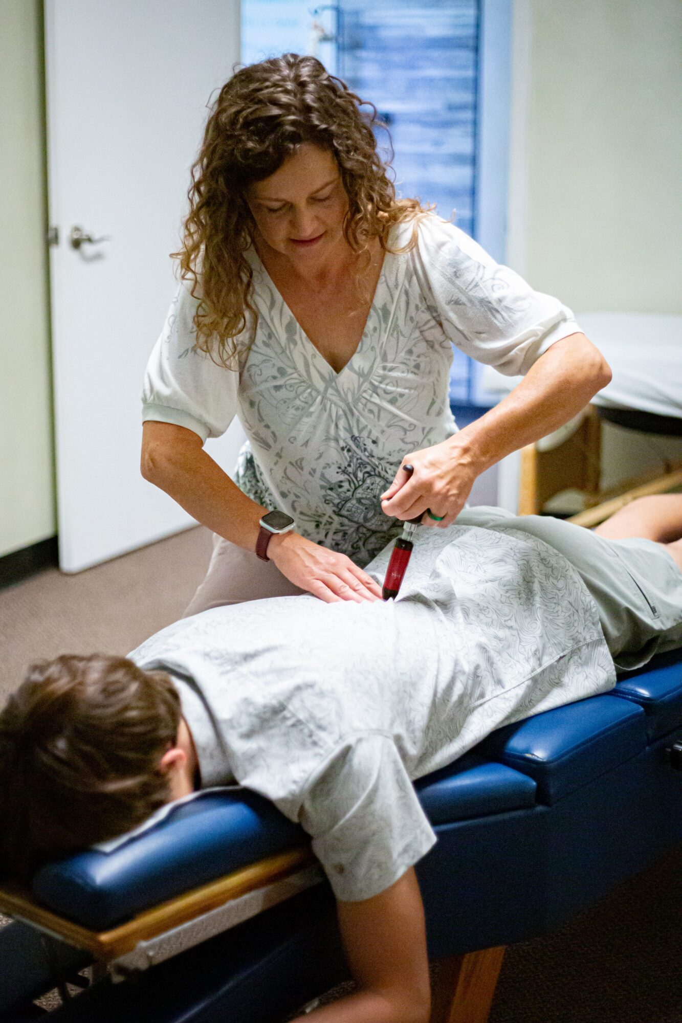 Woman performing a medical procedure on a person lying on an examination table in a clinical setting.