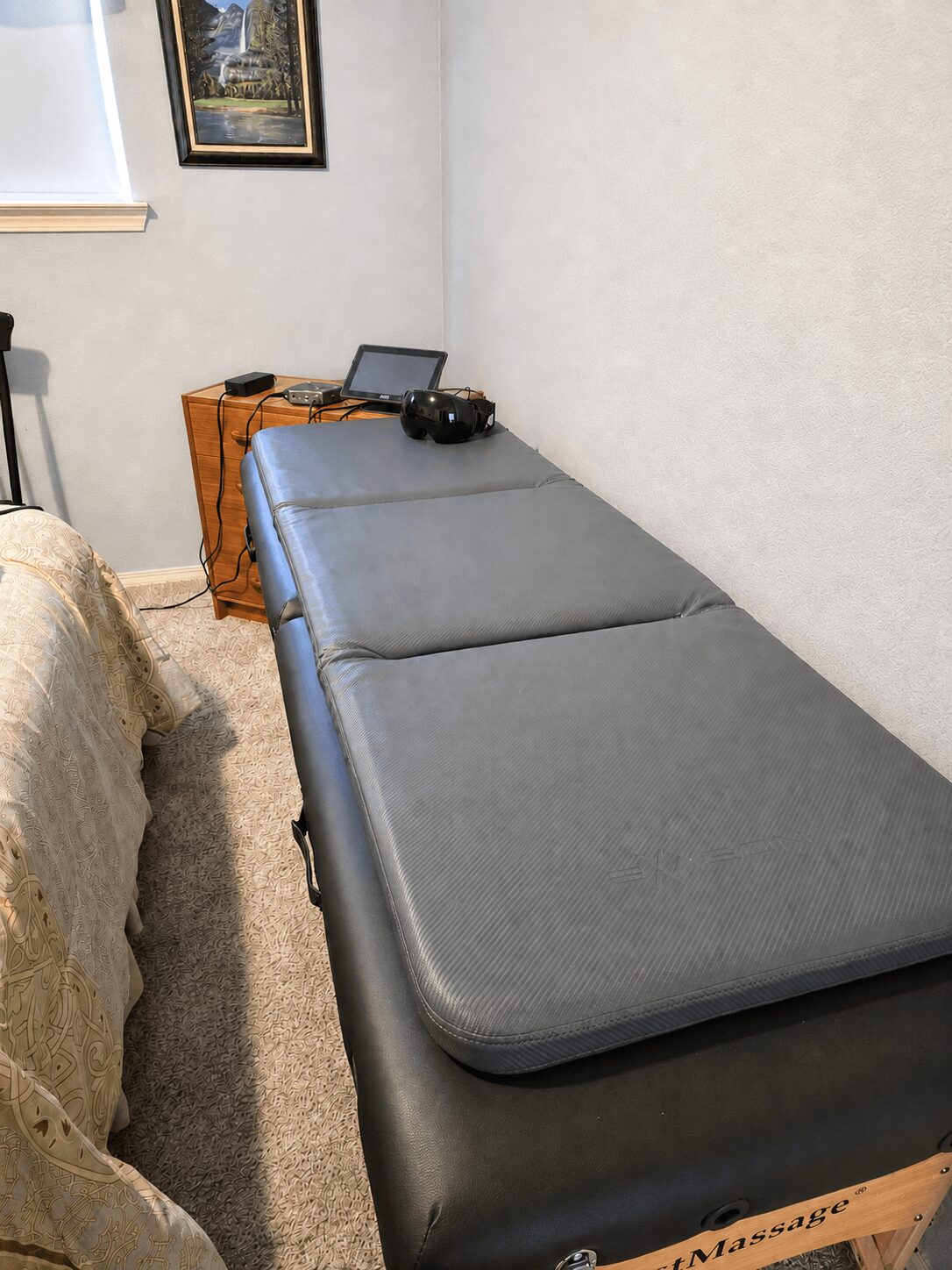Gray cushioned bench against a white wall with a small wooden table and electronic devices on top.