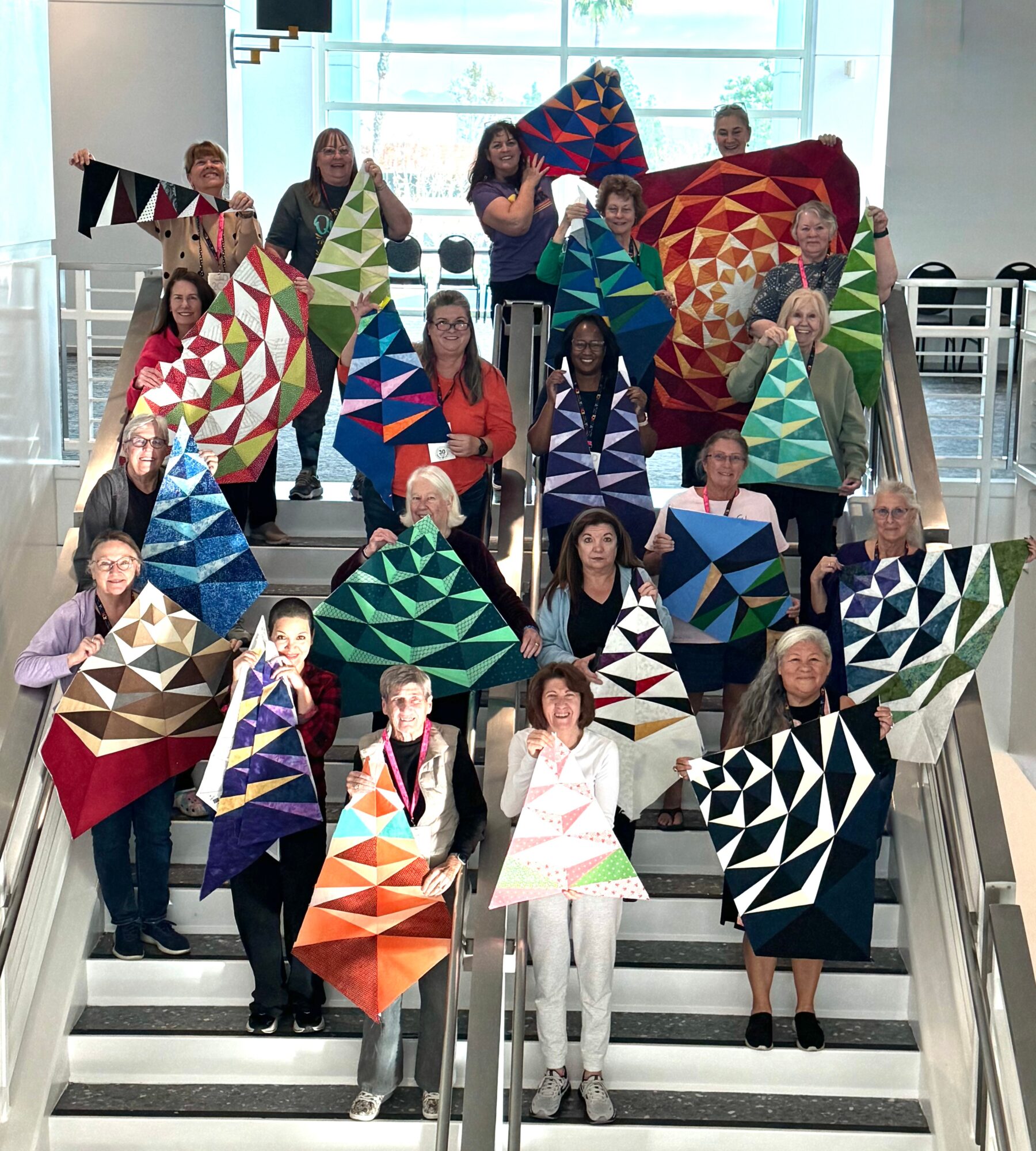 Group of people holding colorful geometric-patterned banners on staircase, with large window in background.