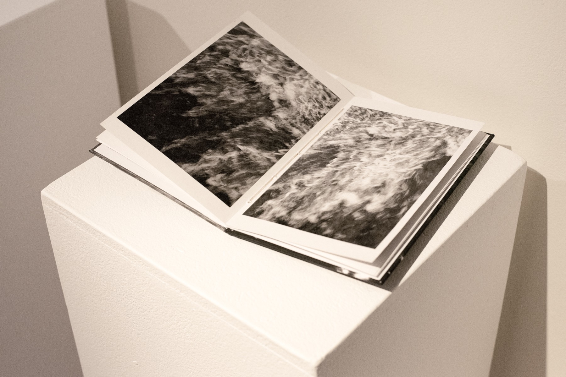 Open photo album with black and white images on a white pedestal, against a plain wall.