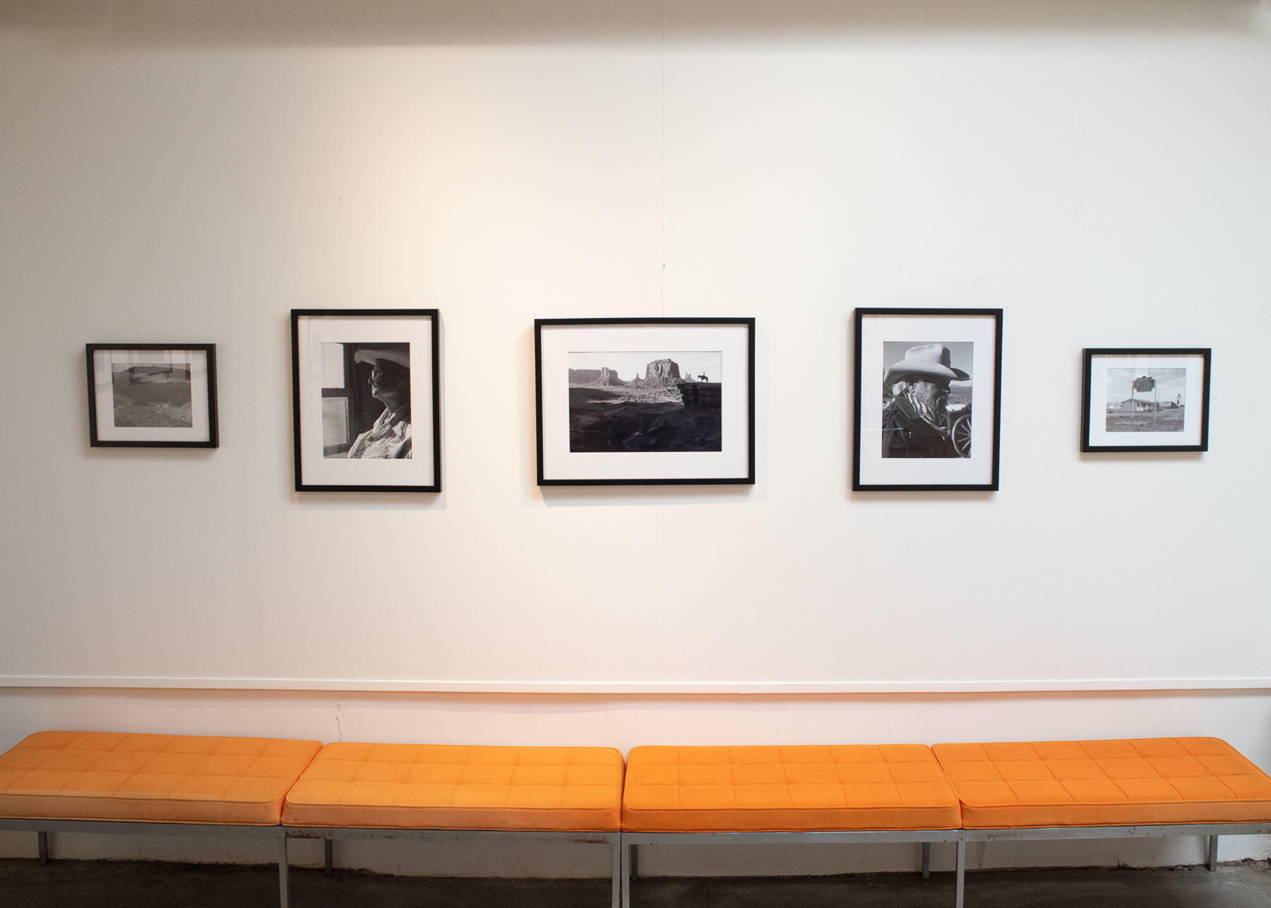Five framed black-and-white photographs hung on a white wall above an orange bench.