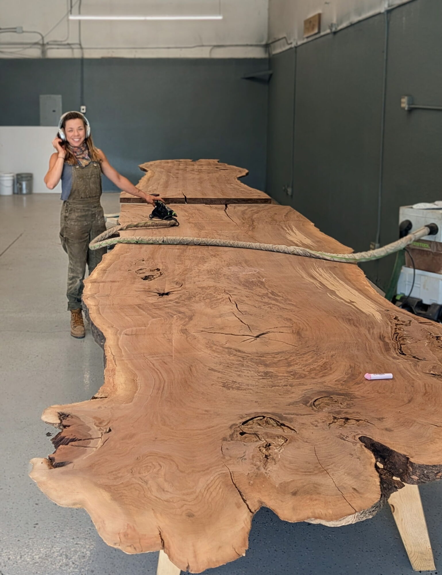 Person standing next to a large, natural wood slab in an indoor space, smiling and holding a phone to their ear.