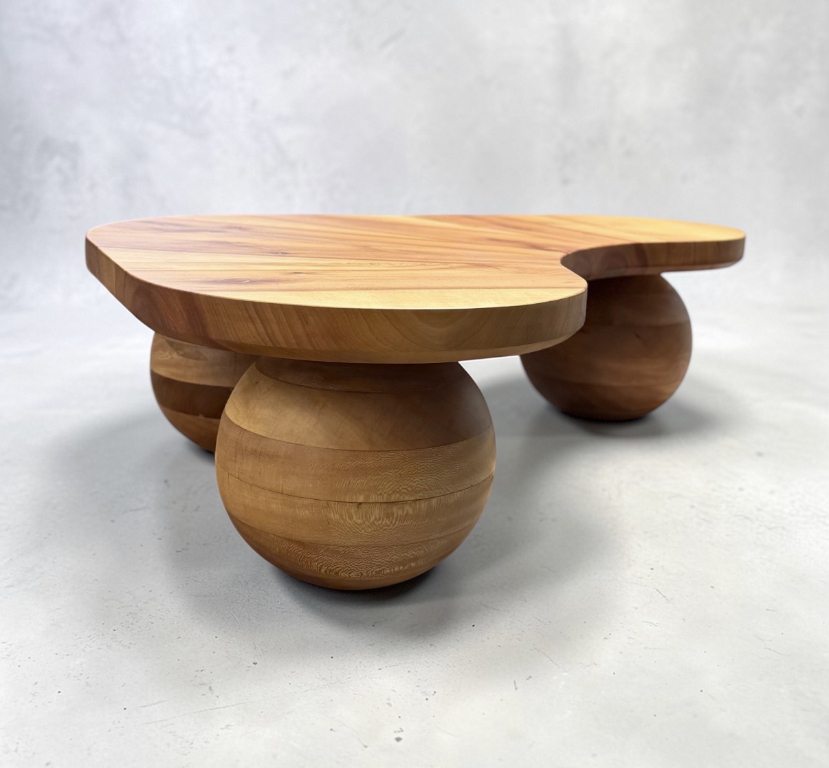 Wooden table with a flat top and three large rounded legs, set against a plain light background.