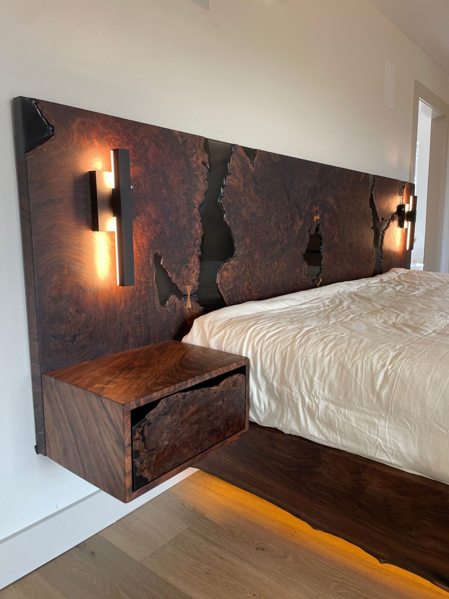 View of a bedroom corner with a bed, nightstand, and wall-mounted lights, seen from a low angle.