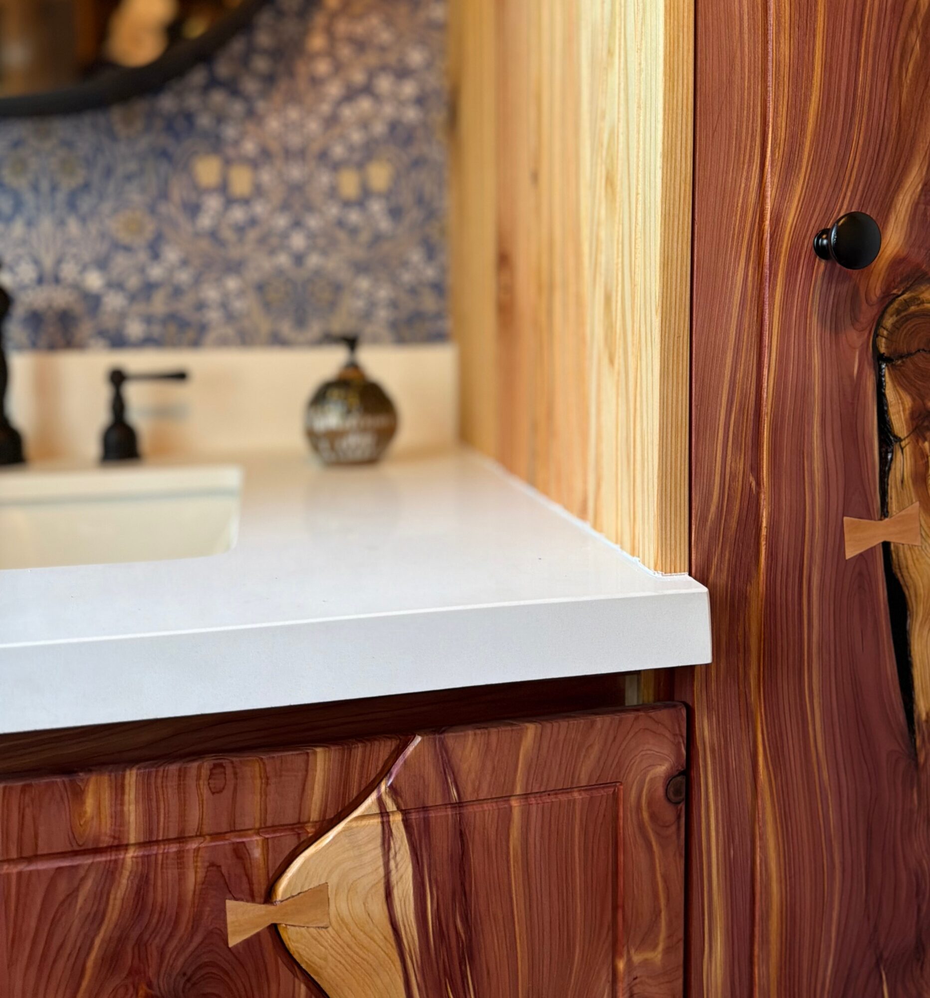 Bathroom vanity with a white countertop, wooden cabinet, and a mirror with a patterned background.