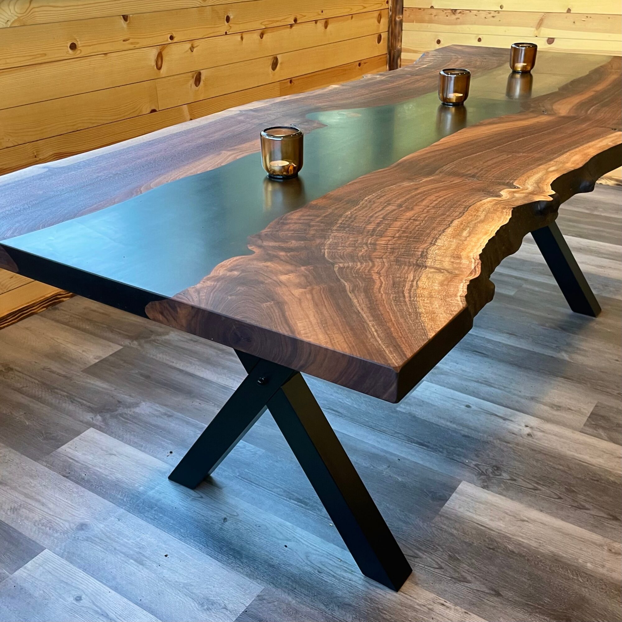 Long wooden table with a natural edge, three metallic cups, in a room with wooden walls and flooring.
