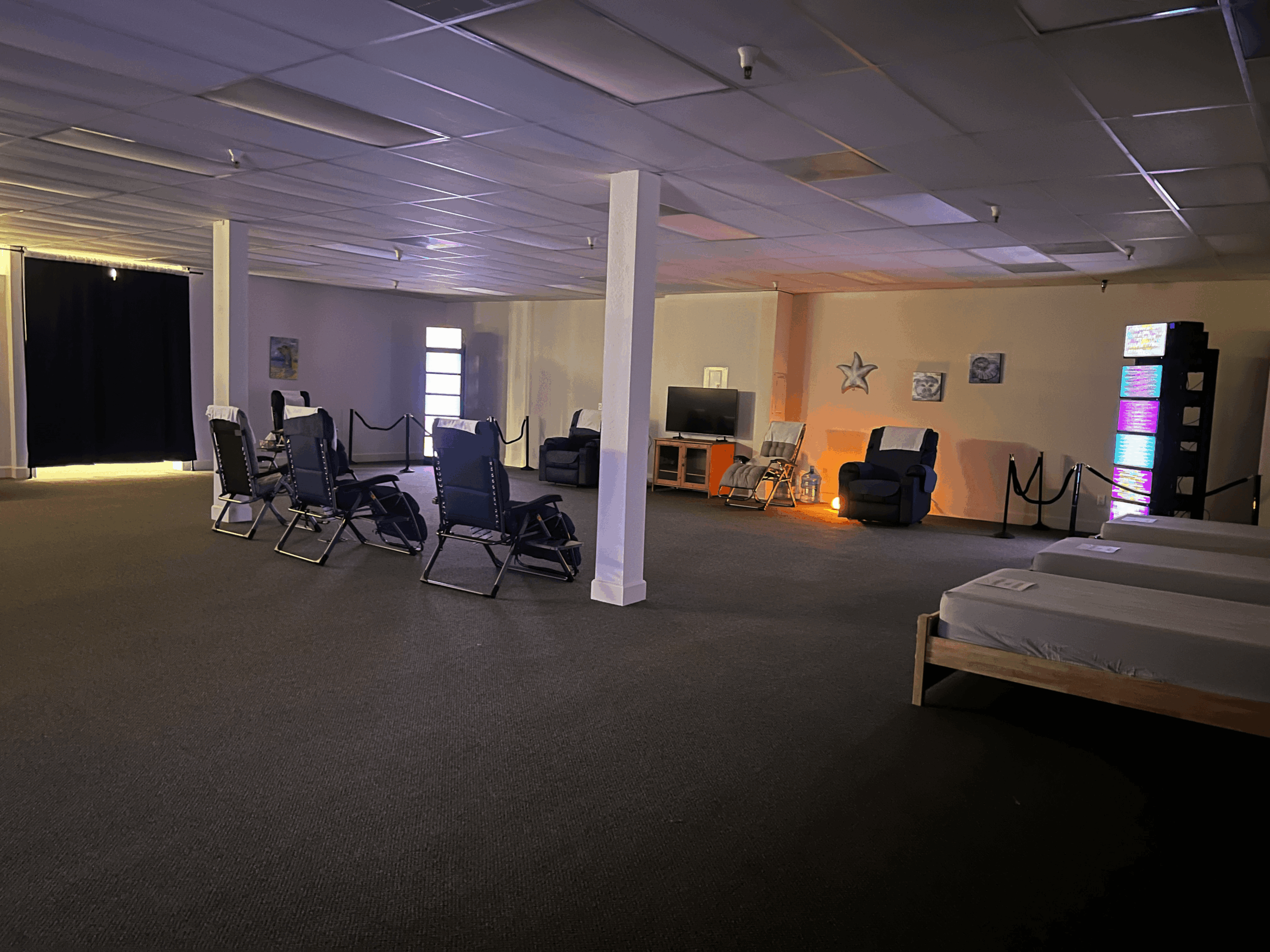 Large room with chairs, a bed, and colorful lighting, decorated with star and picture wall art, dimly lit.