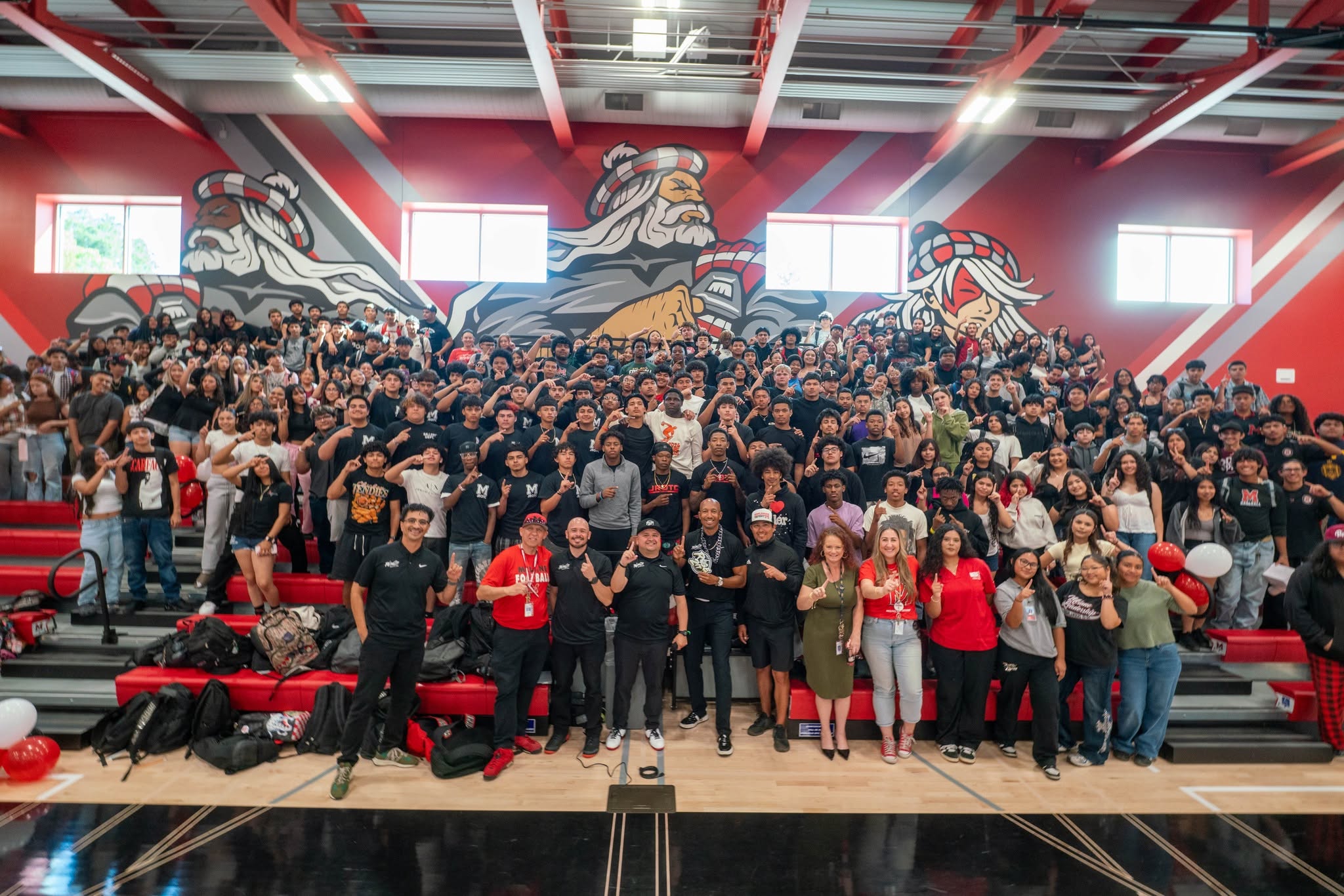 Large group of people gathered in a gymnasium with red walls and murals of animals, posing for a group photo.