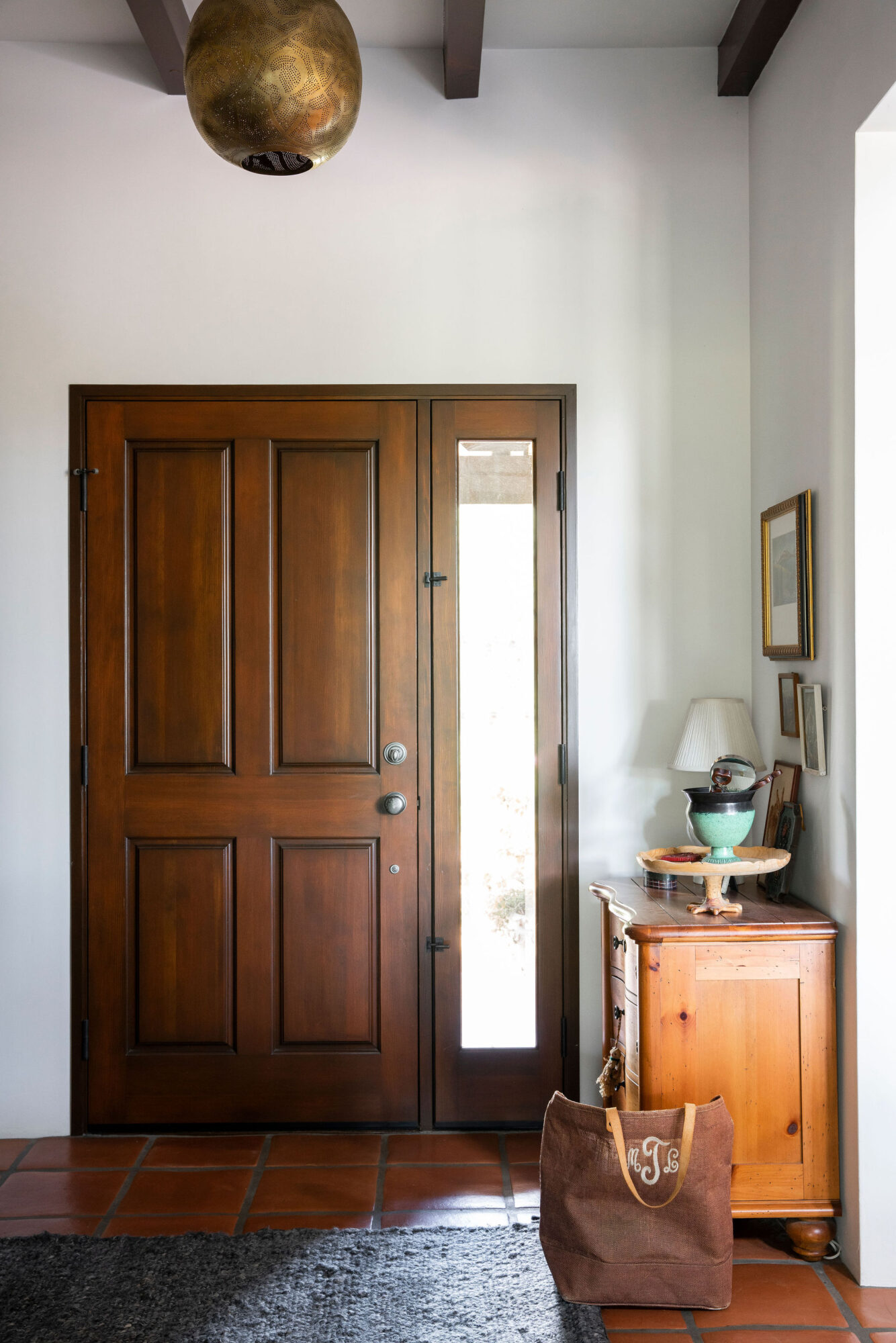 Wooden door with glass panel beside a small wooden cabinet with decorative items, a lamp, and a bag on the floor.