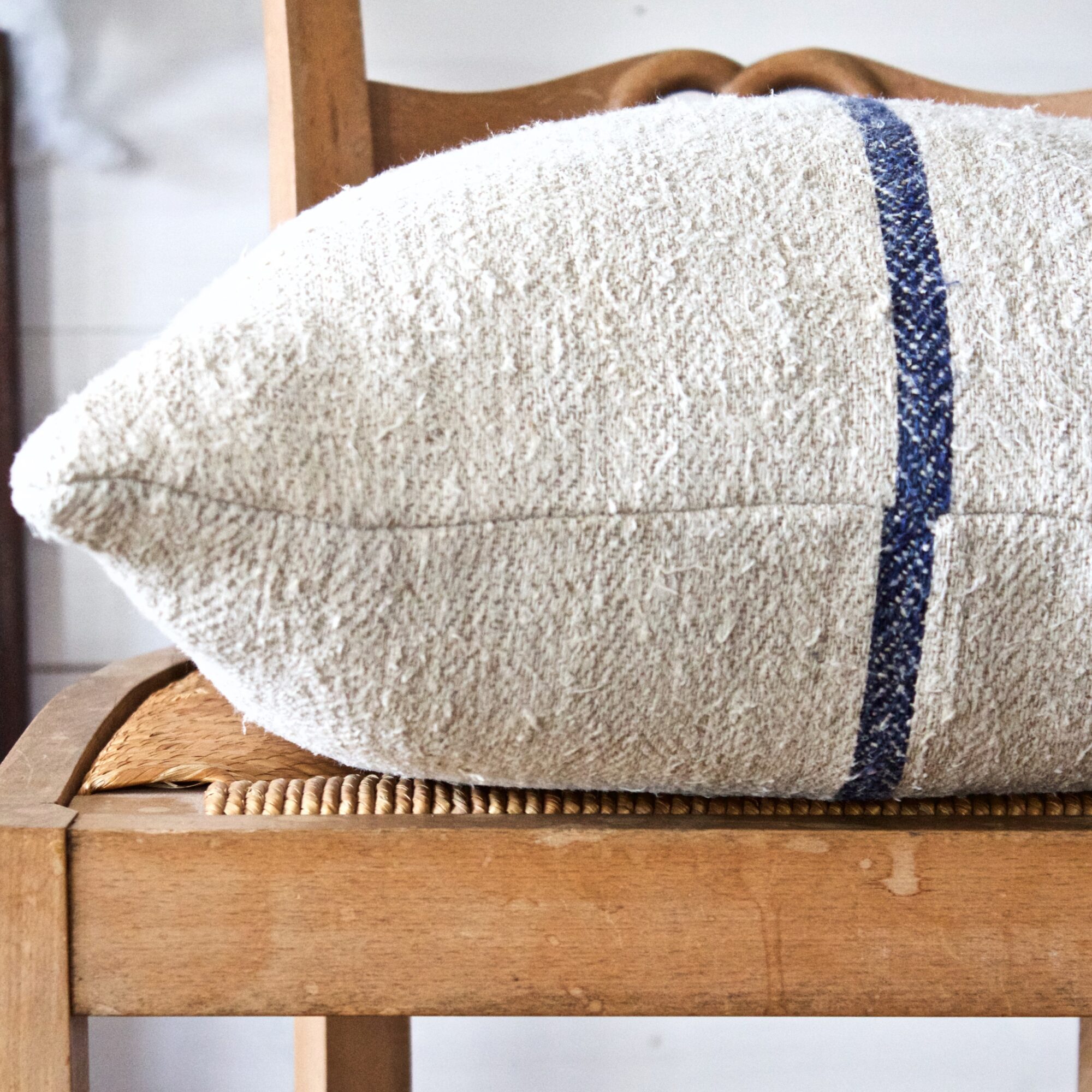 Close-up of a textured white pillow with a blue stripe on a wooden chair.