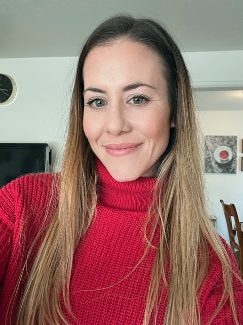 Woman with long hair wearing a red turtleneck sweater, smiling indoors.
