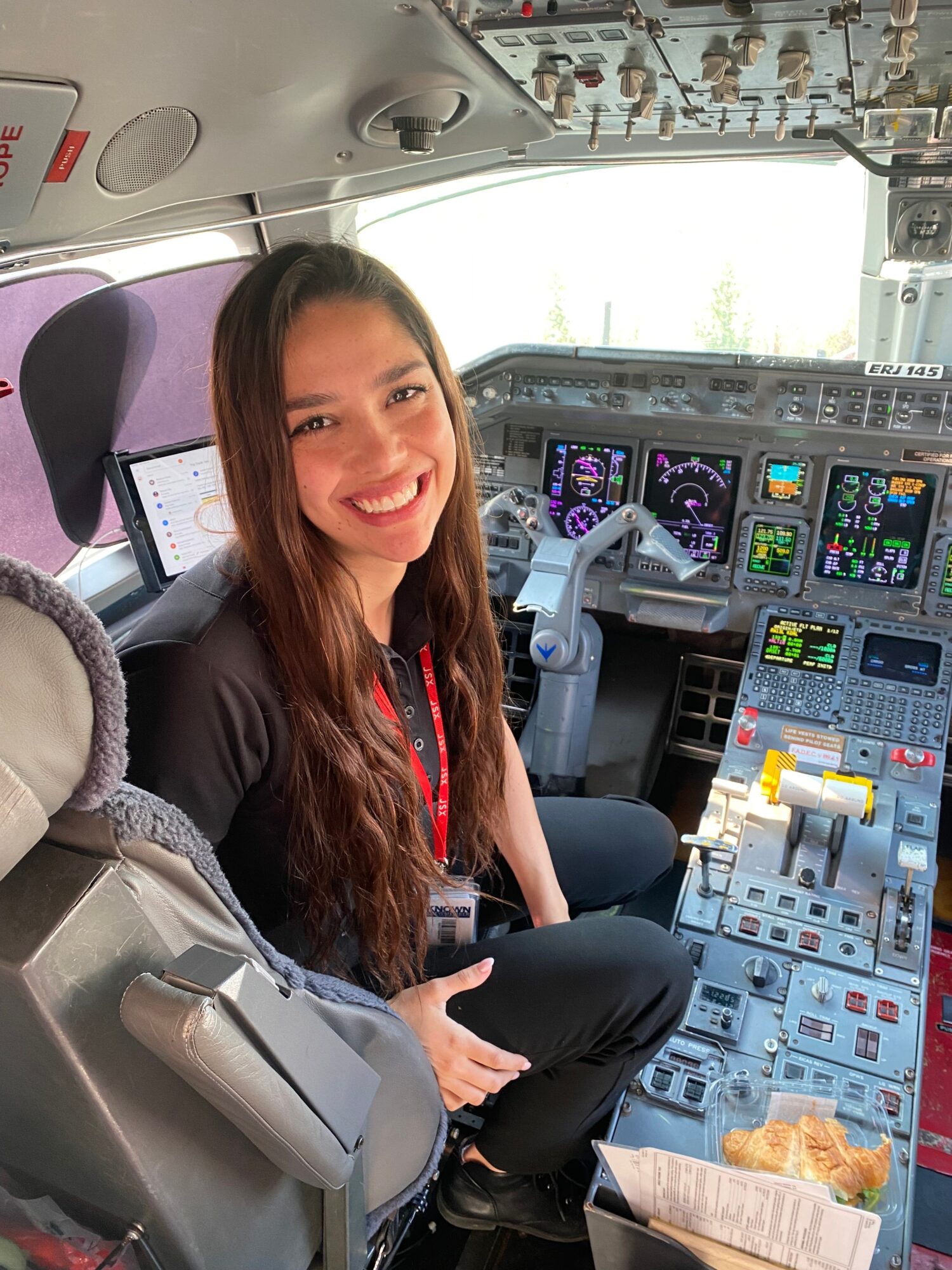 Woman sitting in cockpit with control panels and screens, smiling at camera.