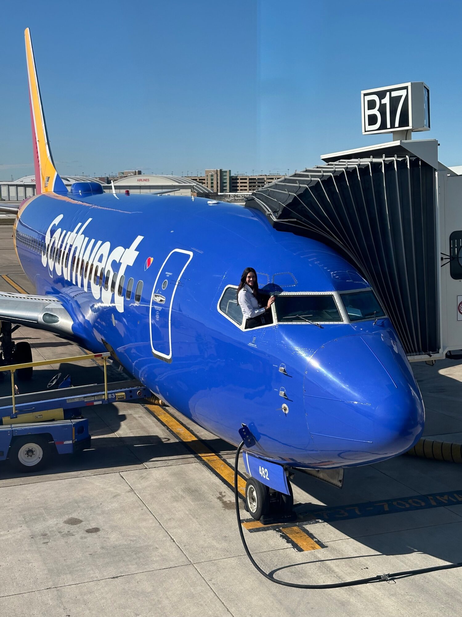 Blue airplane parked at gate with jet bridge attached, on a tarmac under clear sky.