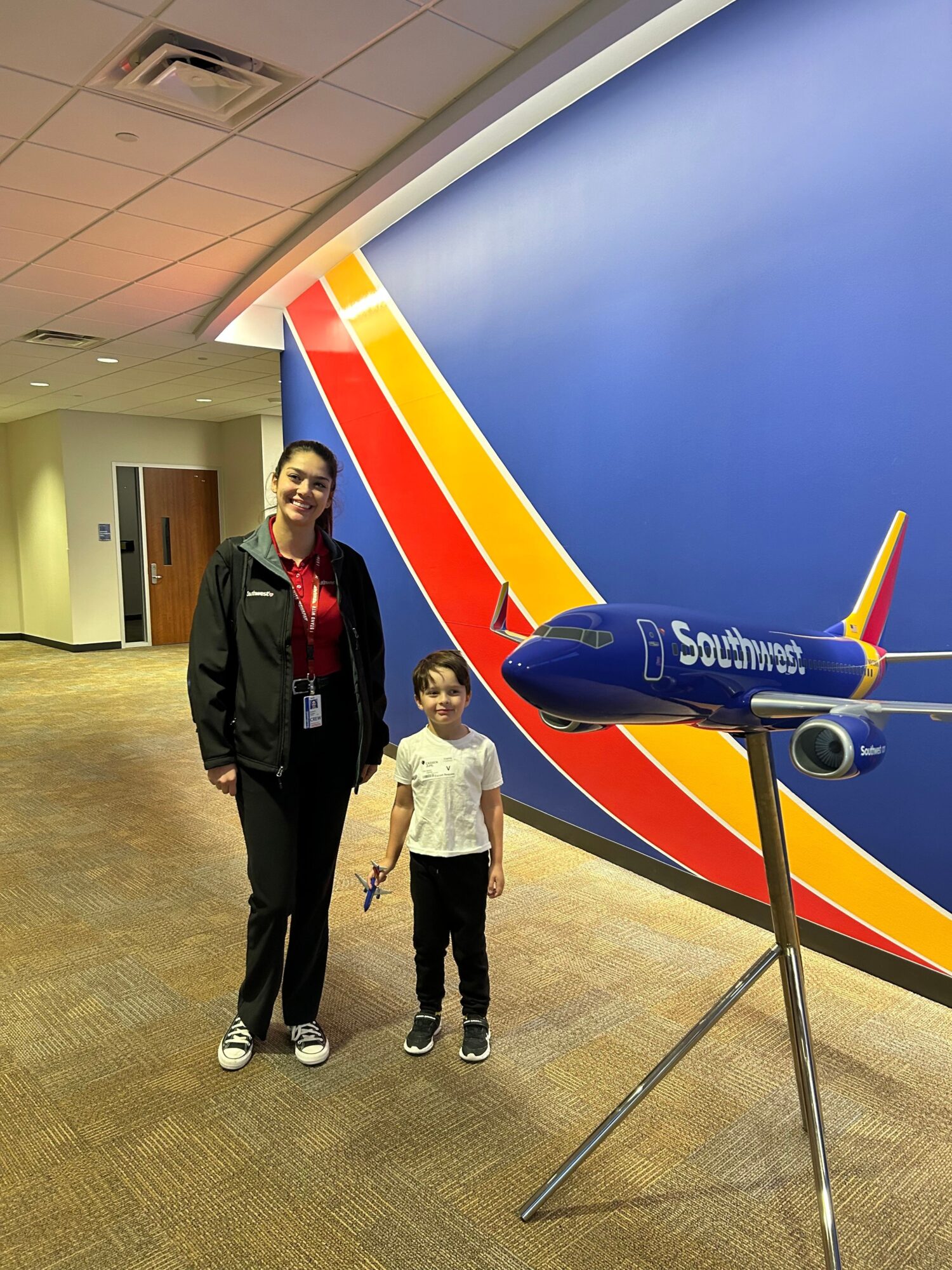 Two people standing in front of a Spirit Airlines airplane model at an indoor exhibit, with a blue sky background.
