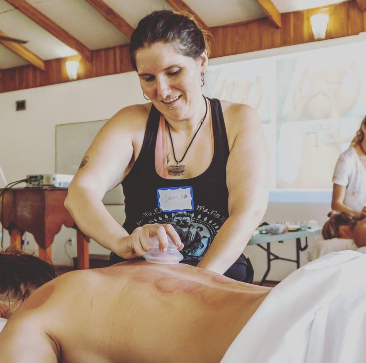 Woman smiling while performing a massage on a person's back in a room with wooden ceiling beams.