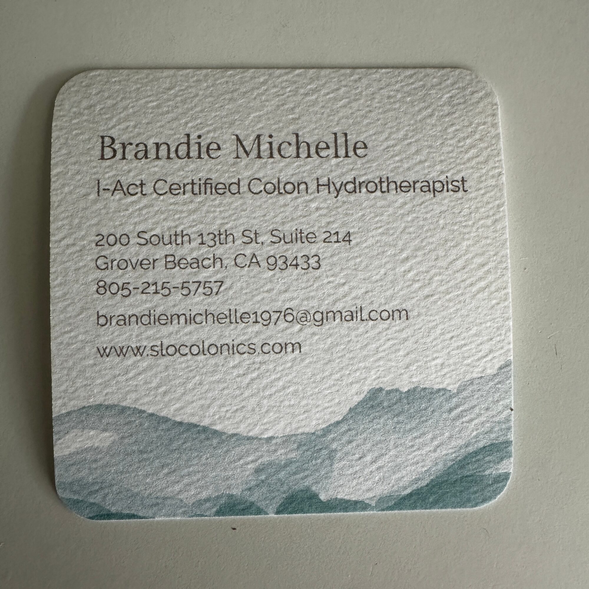 Business card with contact information and a mountain landscape design at the bottom.