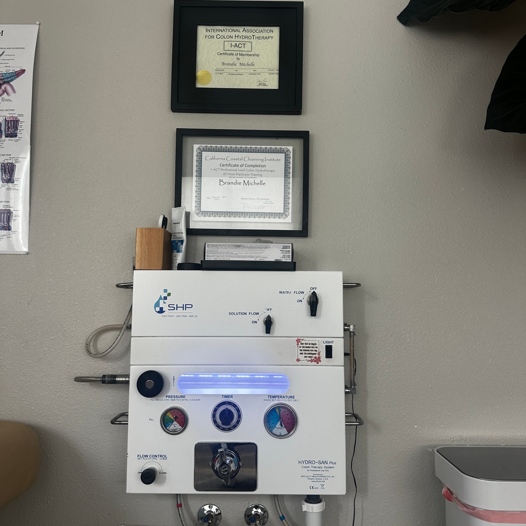 Medical equipment with framed certificates on a wall, a white device with controls, and a small container on the right.