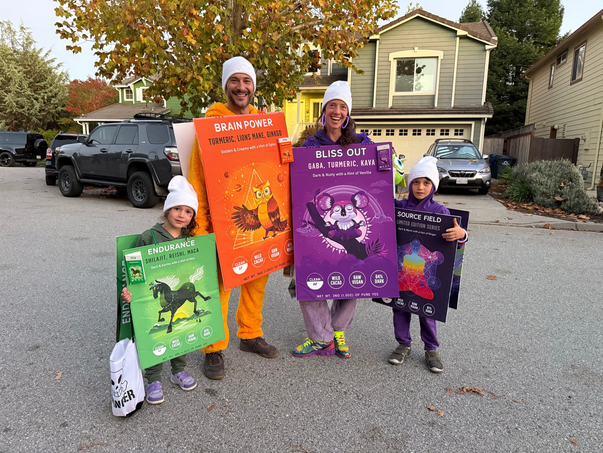 Four children holding colorful educational posters outdoors on a street with houses and trees in the background.