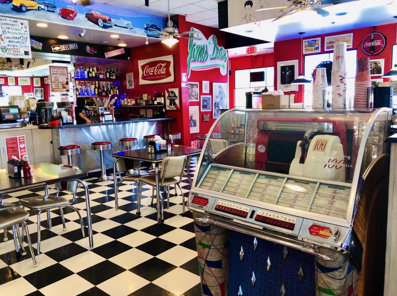 Interior of a retro-style ice cream shop with checkered floor, ice cream freezer, and colorful decor.