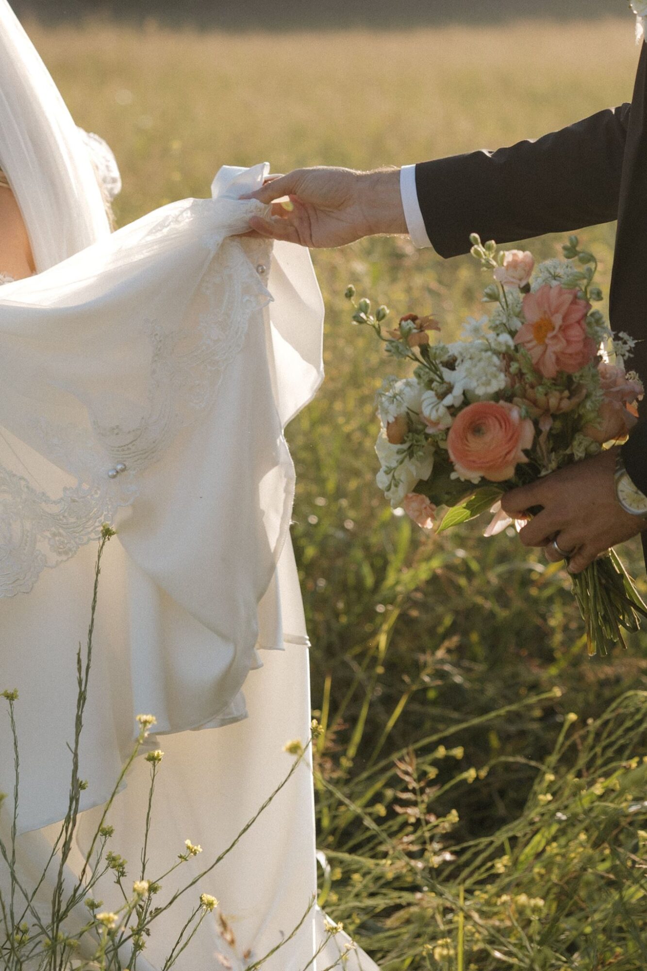 Person holding a wedding dress with a bouquet of flowers in a grassy outdoor setting.