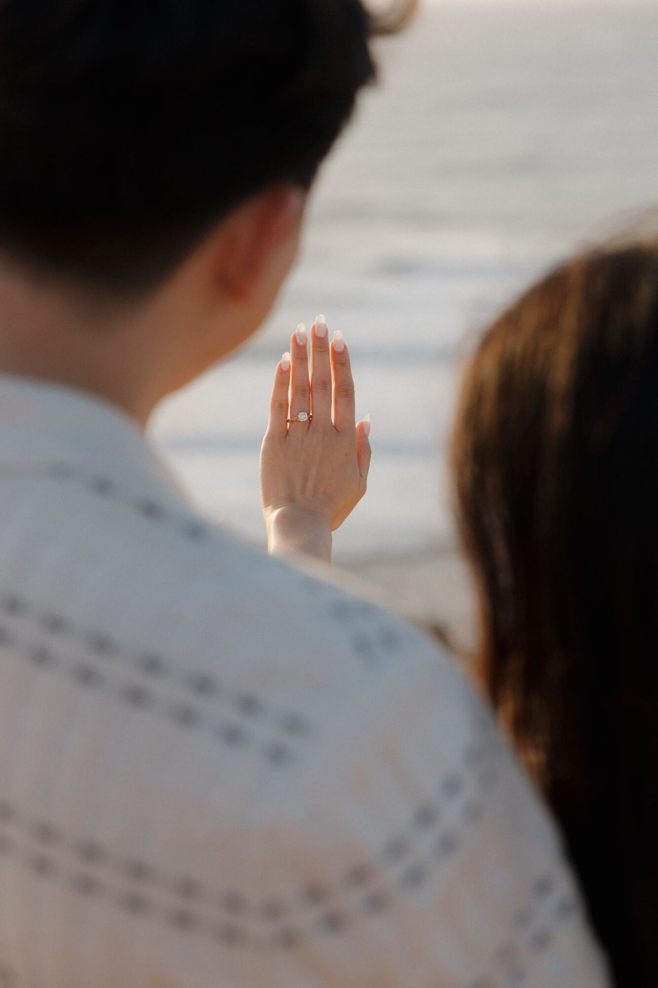 Person with hand raised near water, with two other people in foreground, ocean in background.
