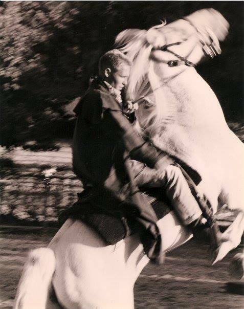 Child riding a horse, holding the reins, with trees in the background, in black and white.