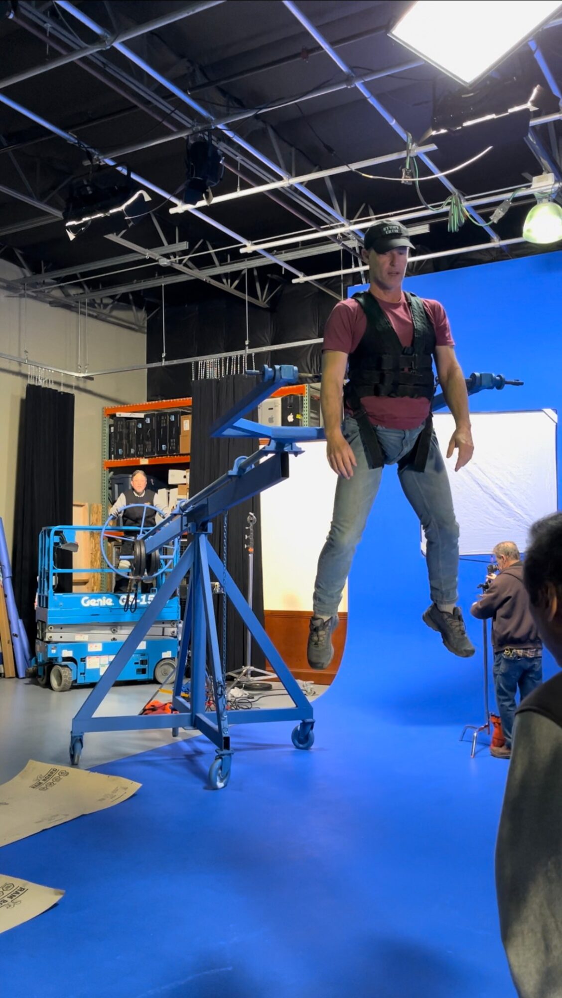 Person wearing a harness and helmet appears to be suspended in a studio with equipment and a blue backdrop.