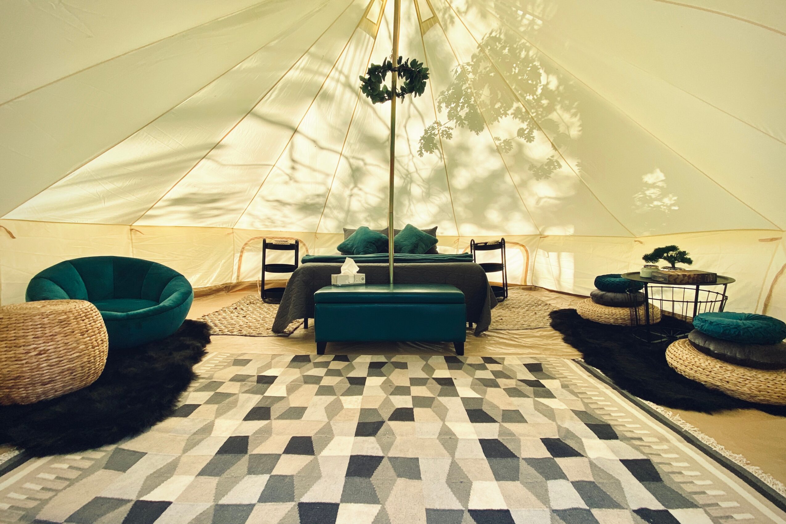 Interior of a tent with seating, a table, and a patterned rug, illuminated by natural light from outside.