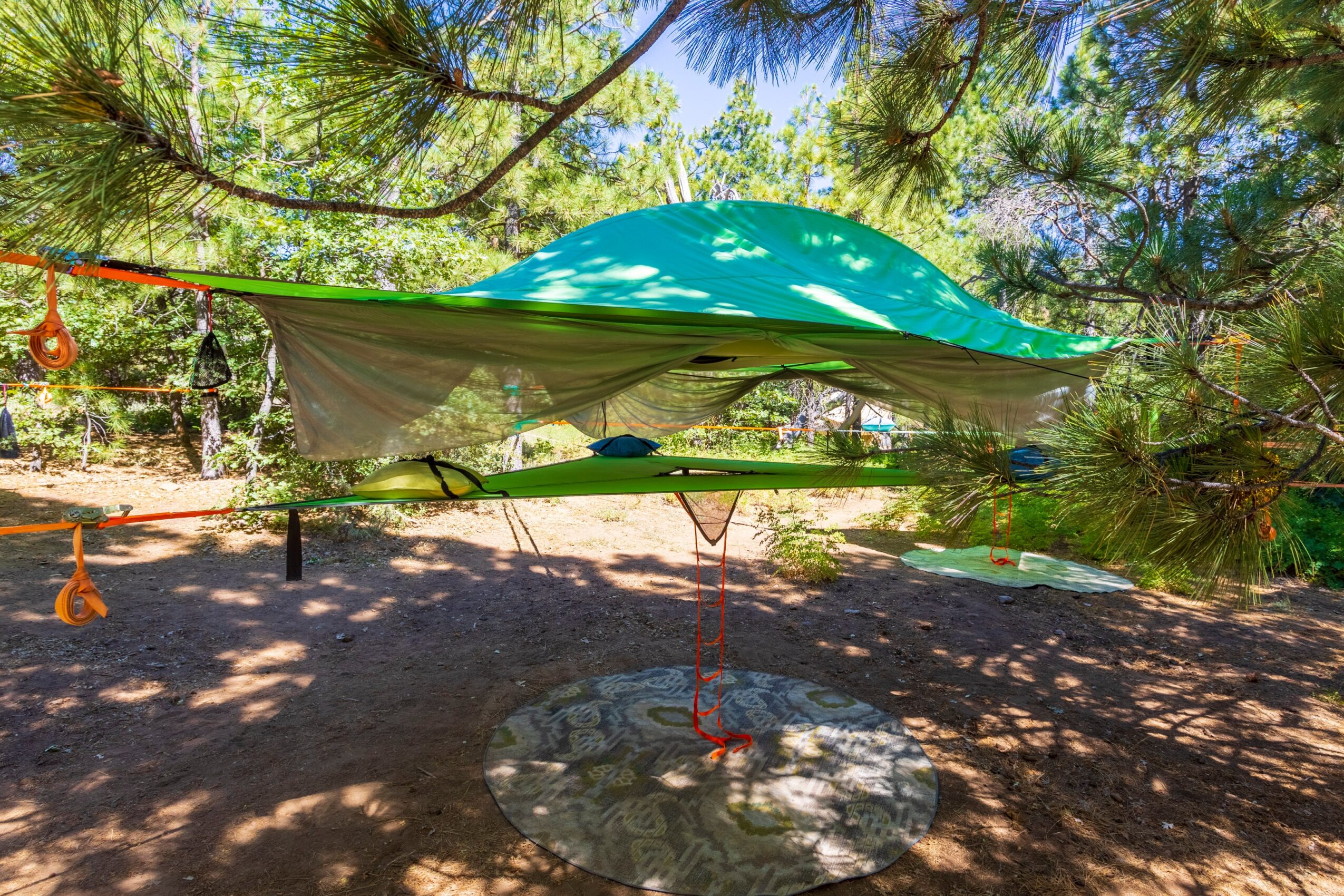 Hammock with a green canopy in a shaded outdoor area among trees, with sunlight filtering through leaves.