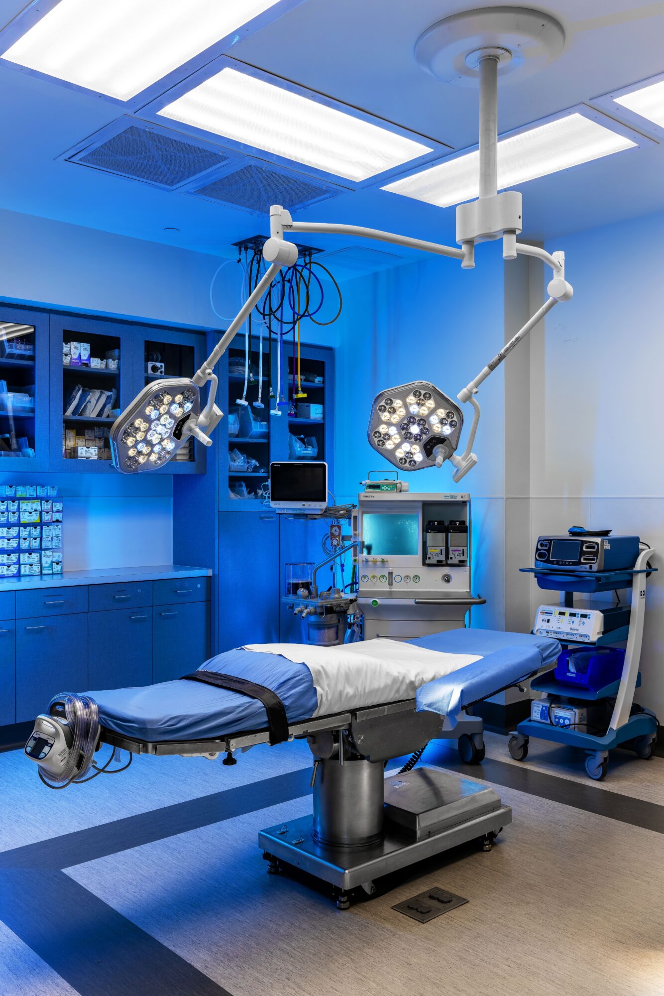 Operating room with surgical lights, an adjustable bed, and medical equipment, all illuminated with bright blue lighting.