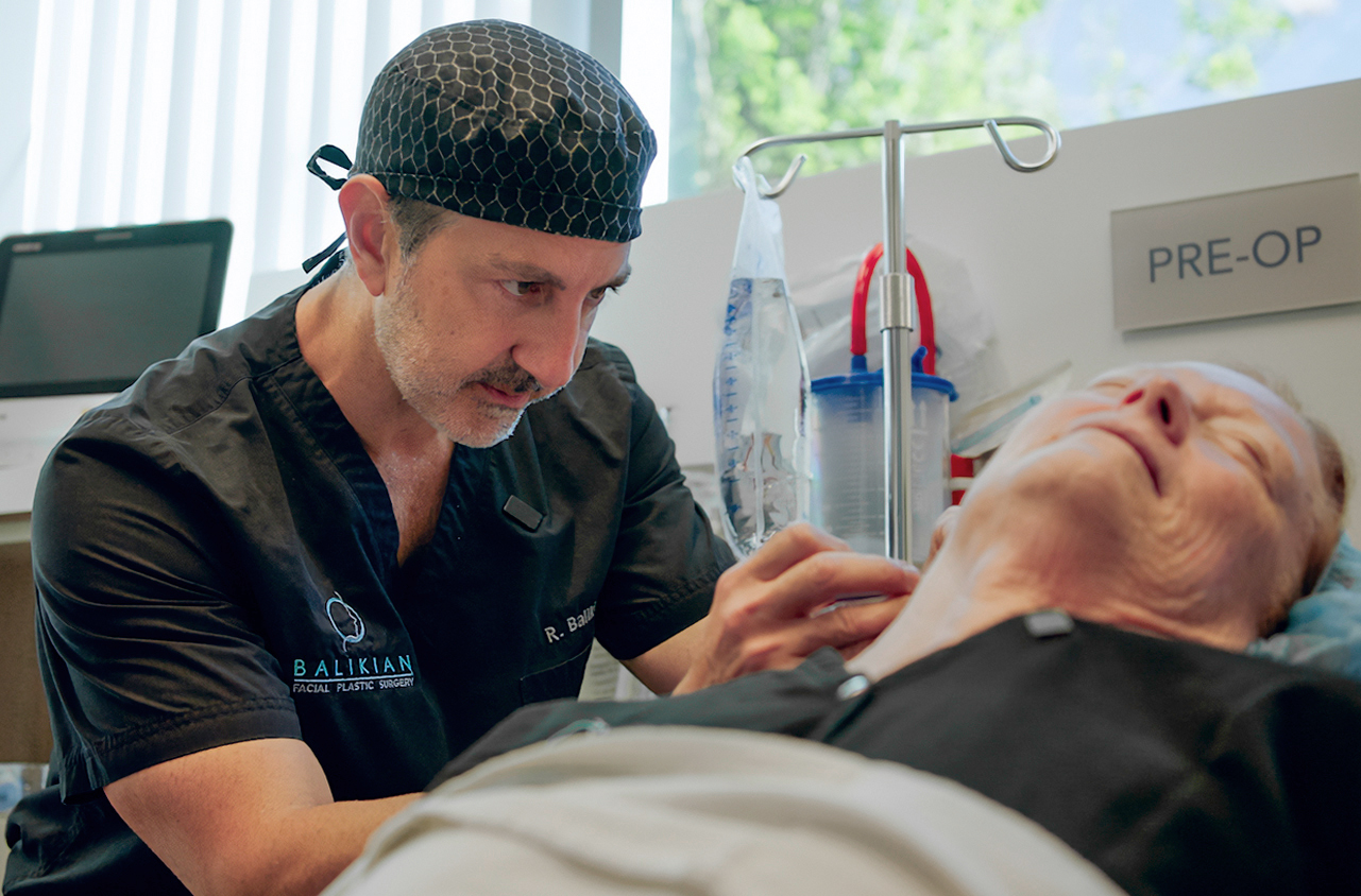 Doctor examining an elderly patient in a hospital room with medical equipment, pre-op sign visible.