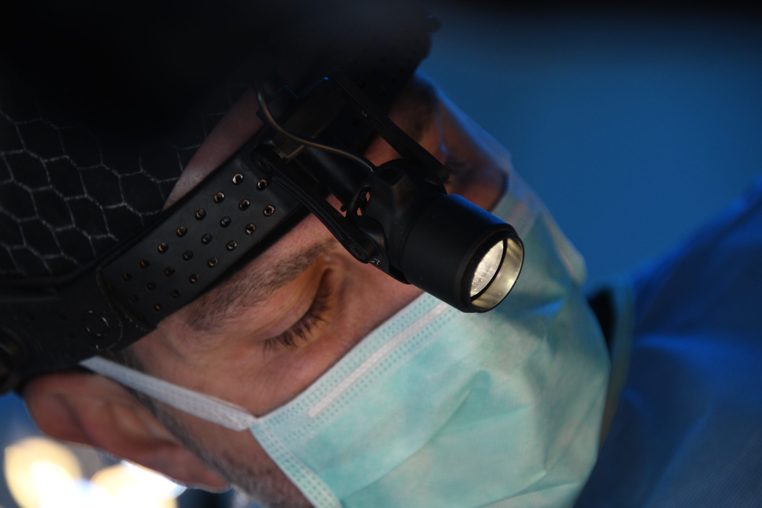 Close-up of a person wearing a headlamp, face mask, and protective clothing, focused on a task.