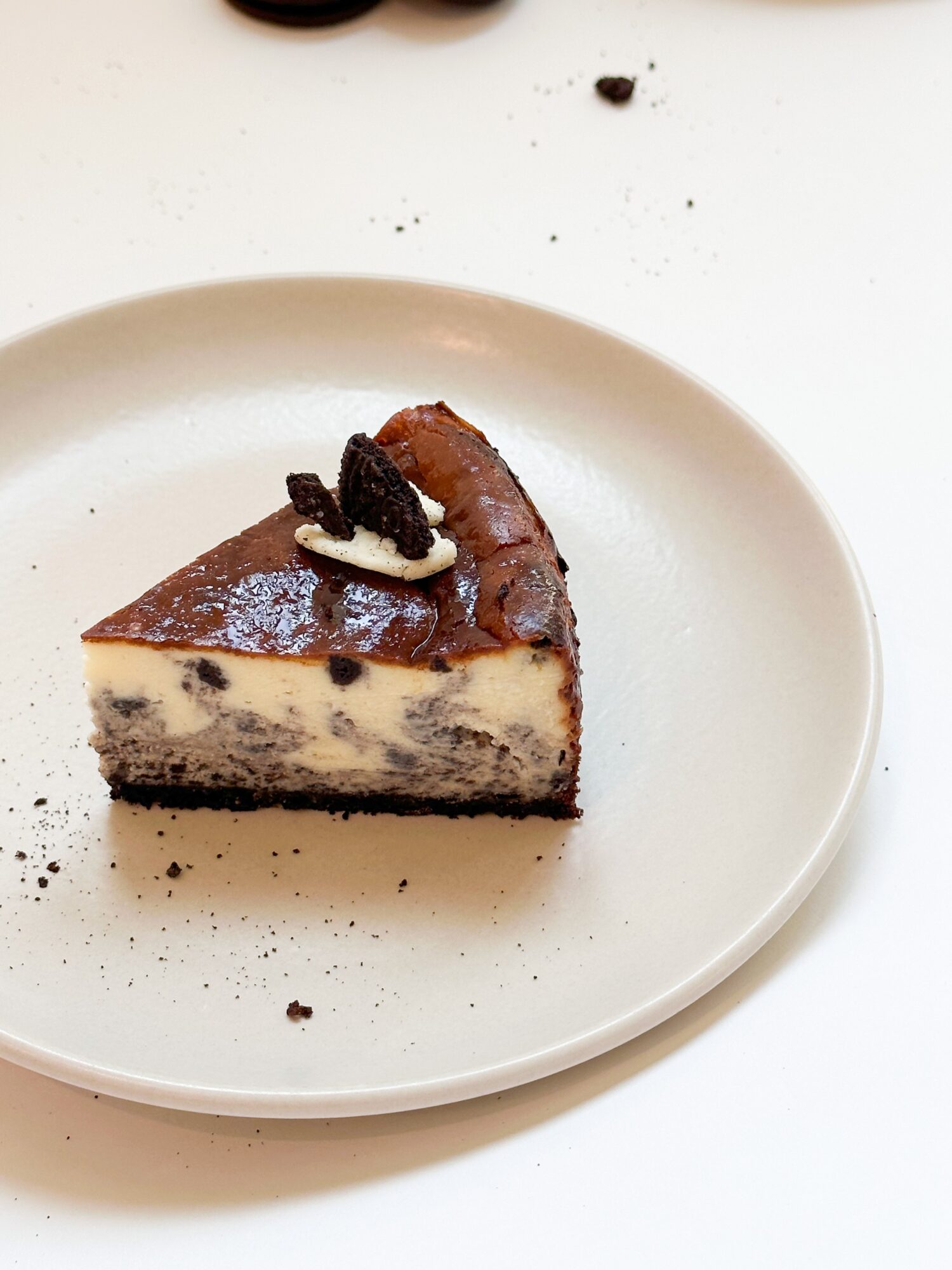 Slice of cookies and cream cheesecake with Oreo topping on a white plate, with crumbs around it.
