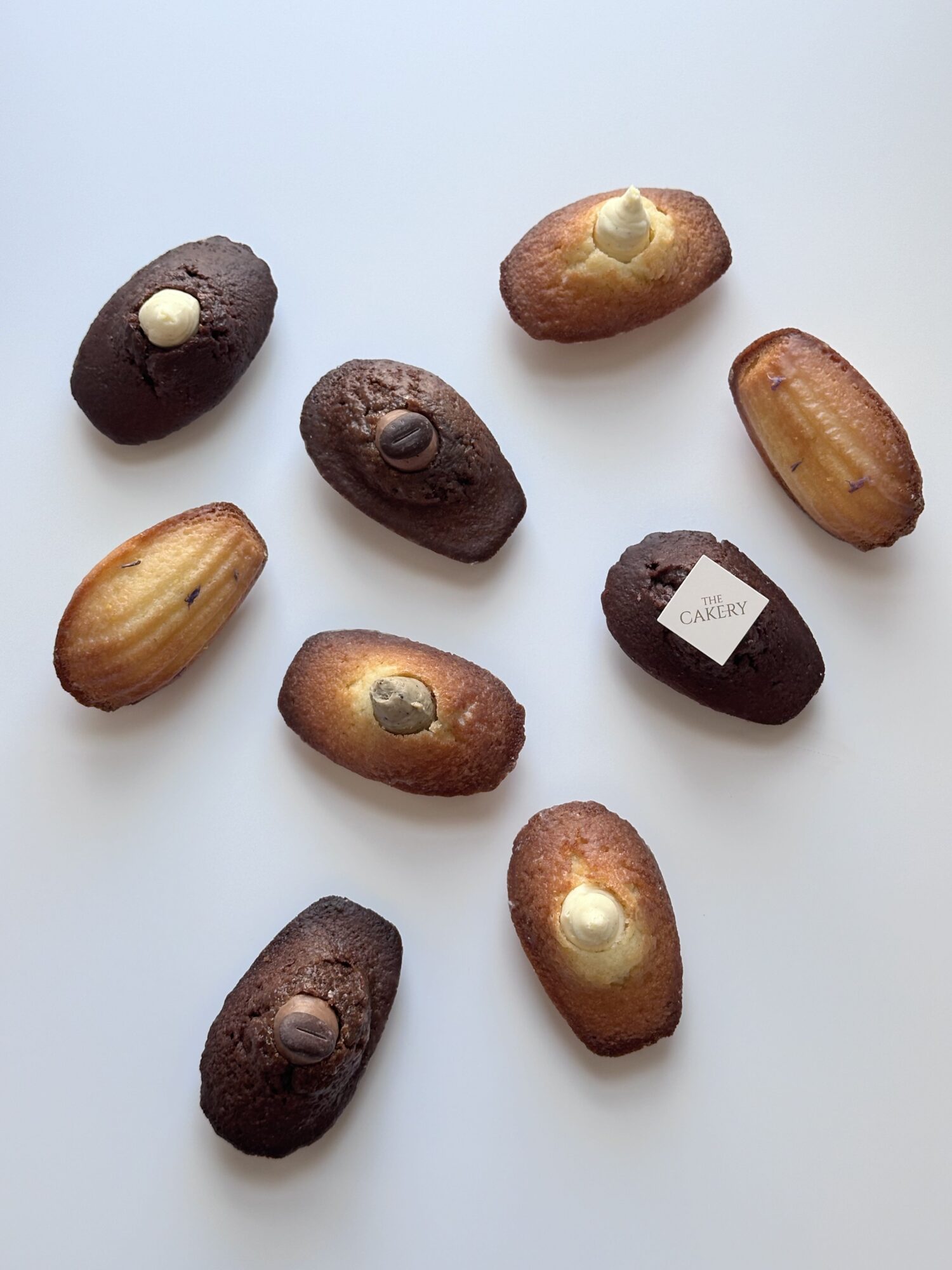 Nine small, oval-shaped baked goods with various toppings and fillings, scattered on a white surface.