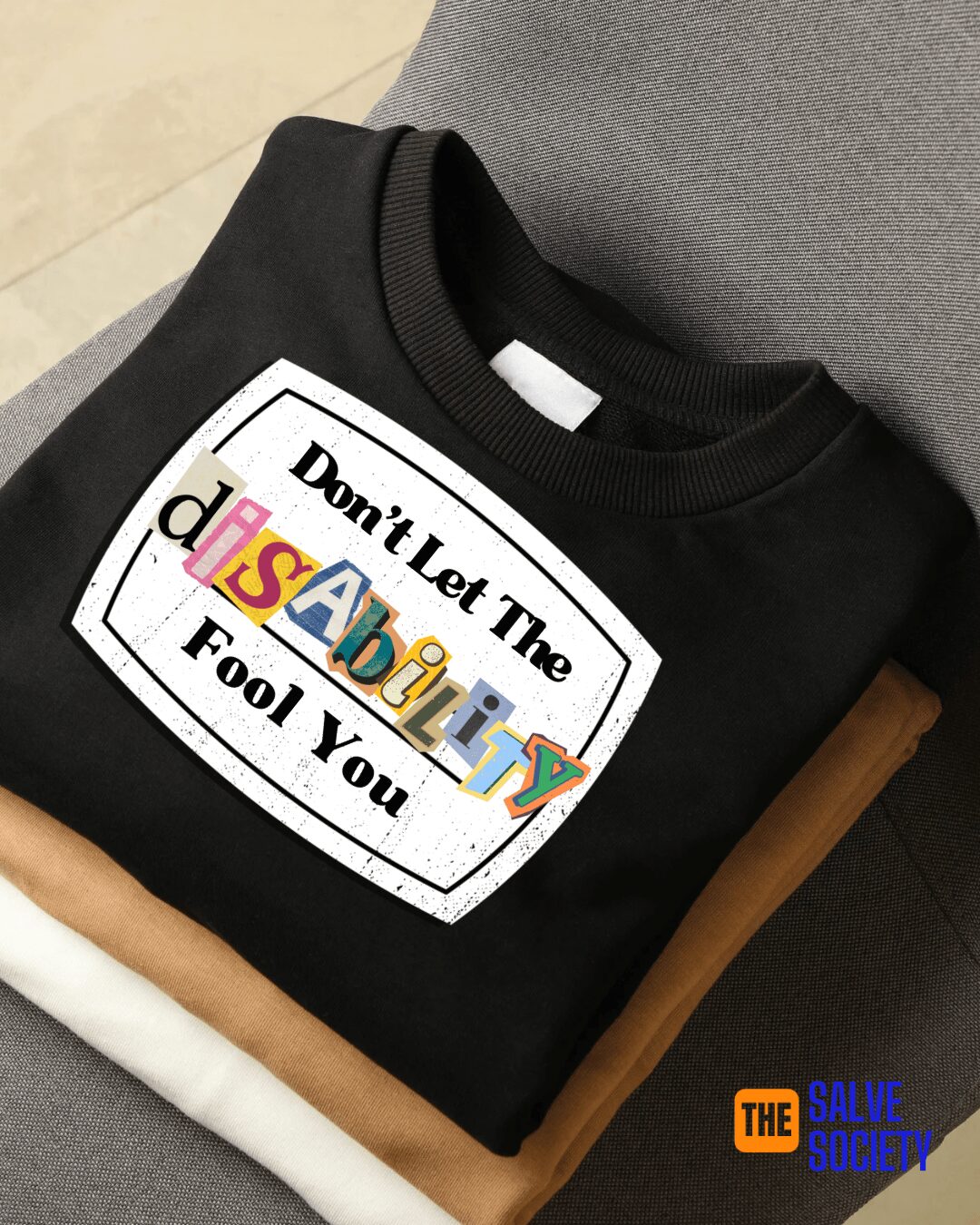 Black sweatshirt with a colorful printed message, folded on a surface with other folded clothes nearby.
