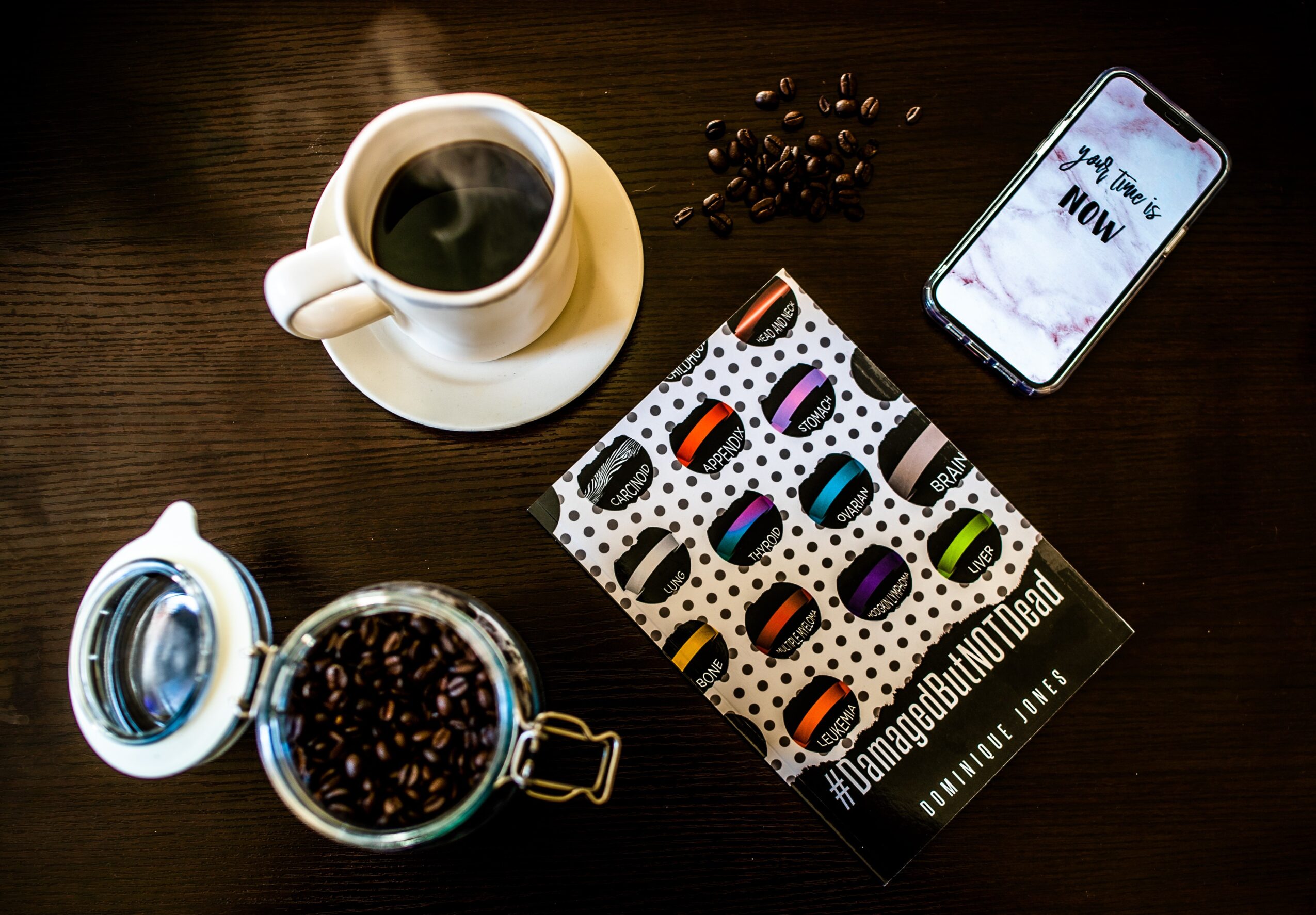 Coffee cup, smartphone, and a box of colorful macarons on a wooden table.