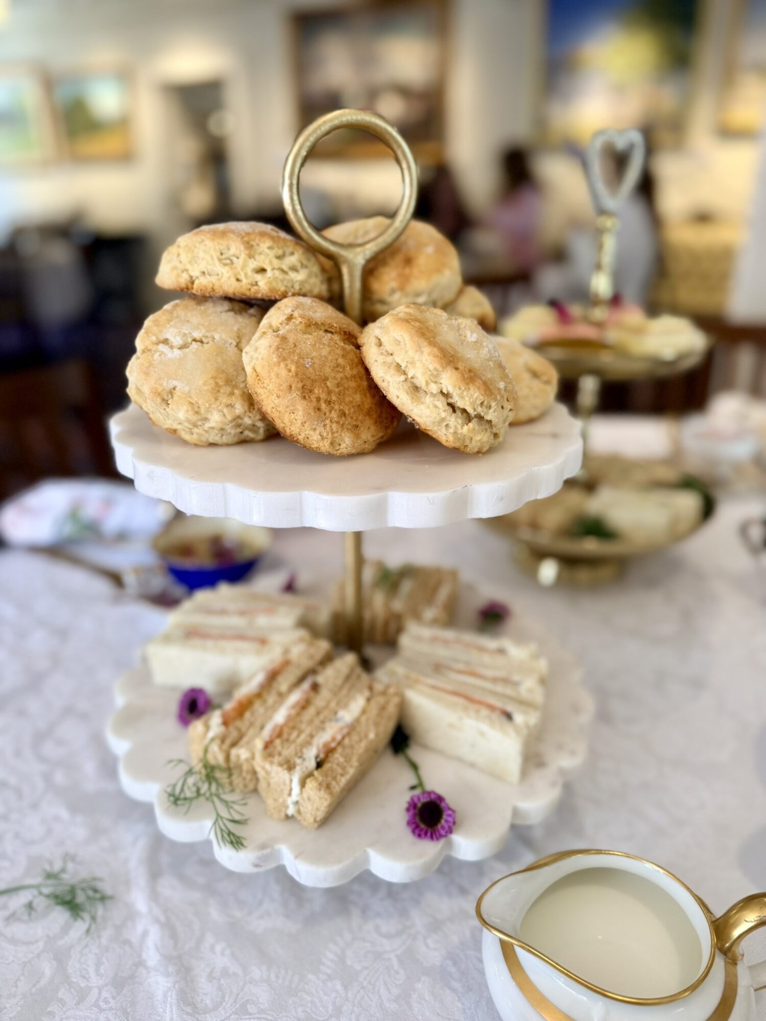 Two-tiered stand with scones on top and finger sandwiches on the bottom, set on a table with a white tablecloth.