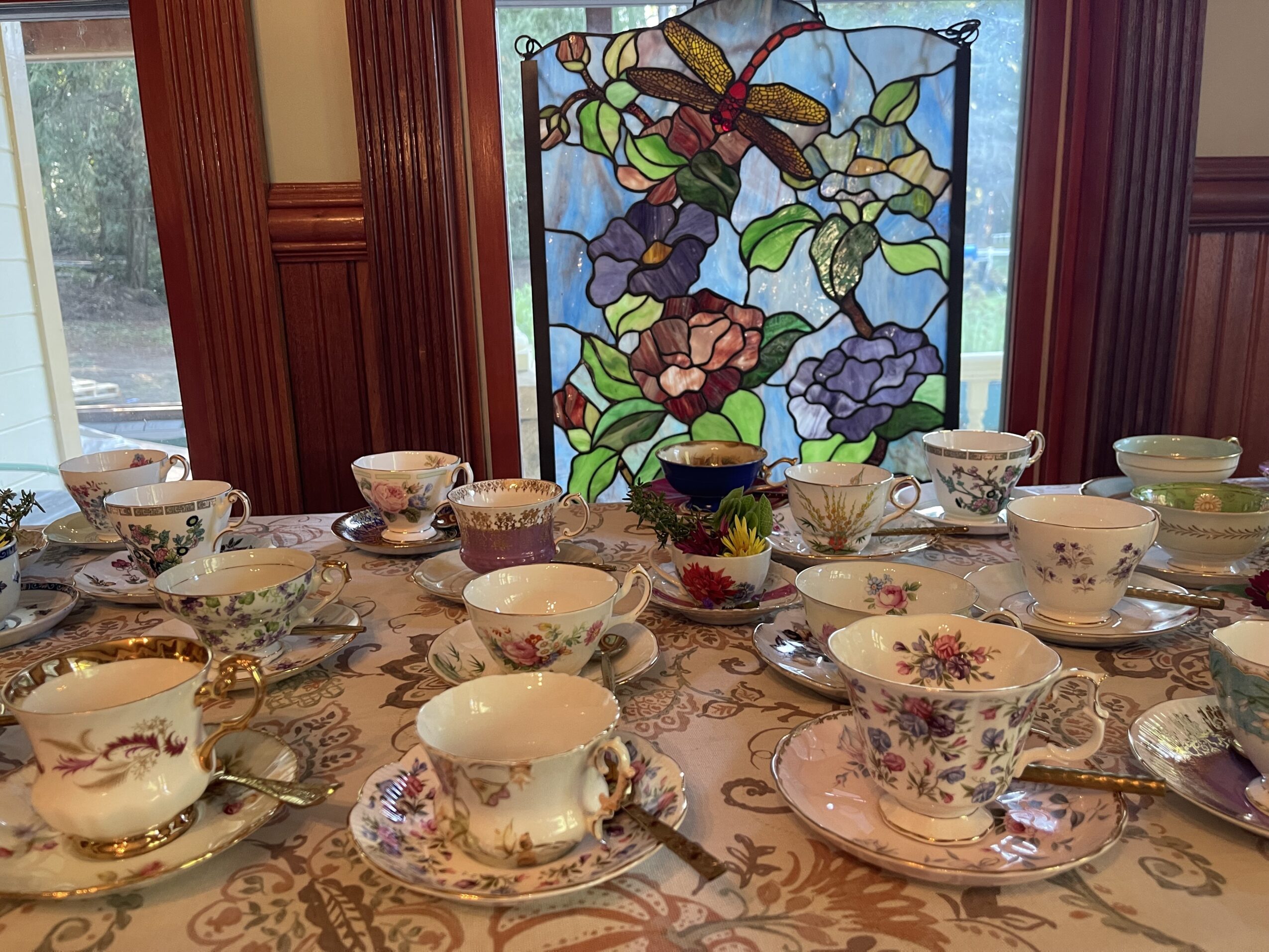 Table with teacups, saucers, and spoons in front of a stained glass window with floral design