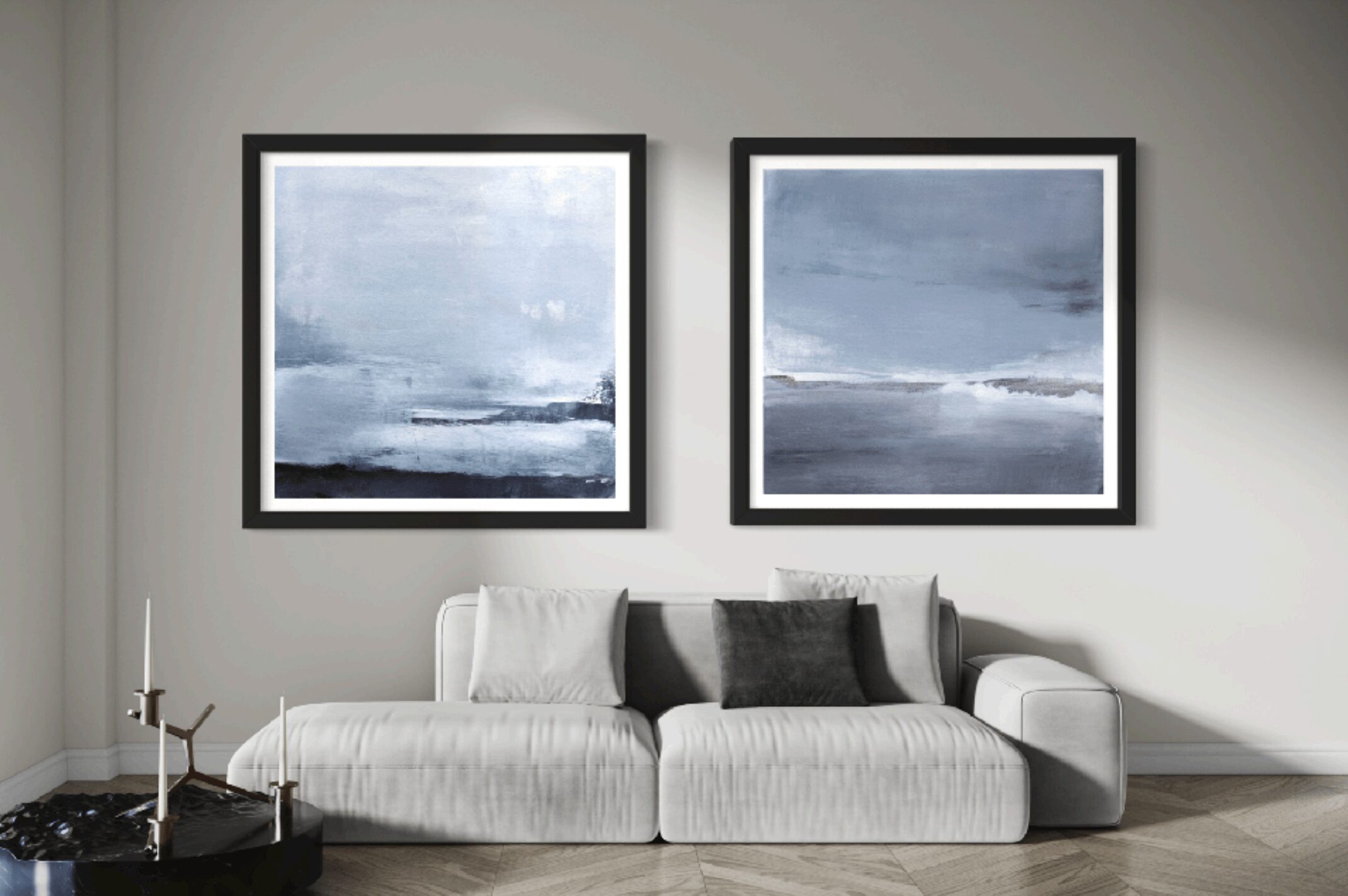 Living room with two framed abstract landscape paintings above a white sofa with black and gray cushions, gray wall background.
