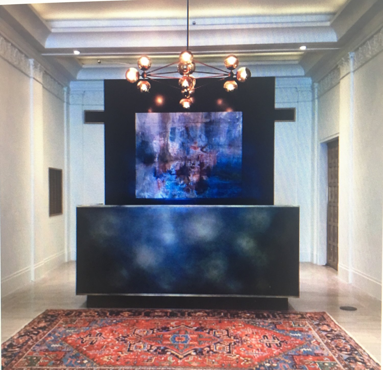 Interior room with a large abstract painting, chandelier, black counter, and a patterned rug.
