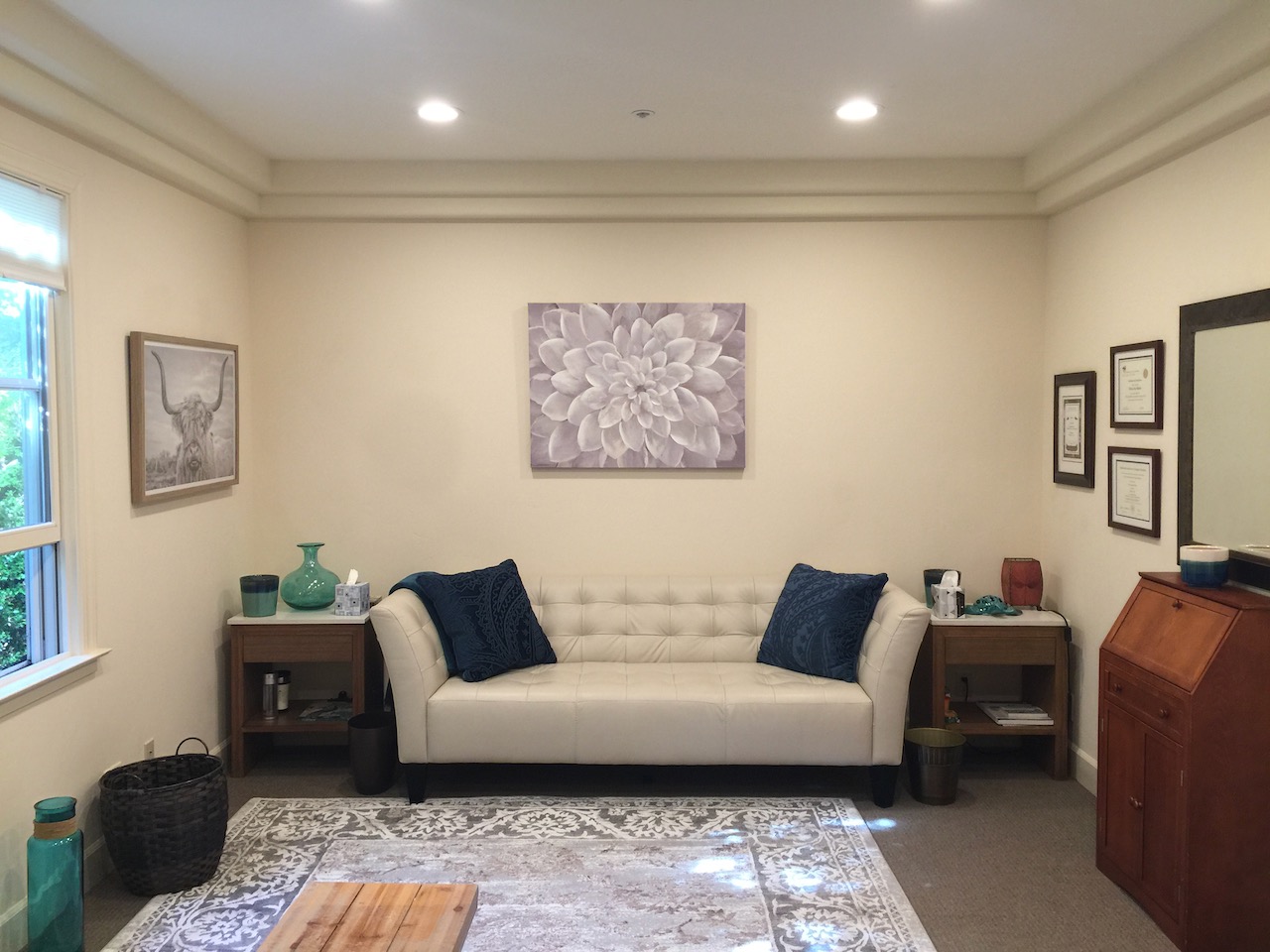 Living room with a white sofa, two side tables, and wall art, illuminated by ceiling lights and natural light from windows.