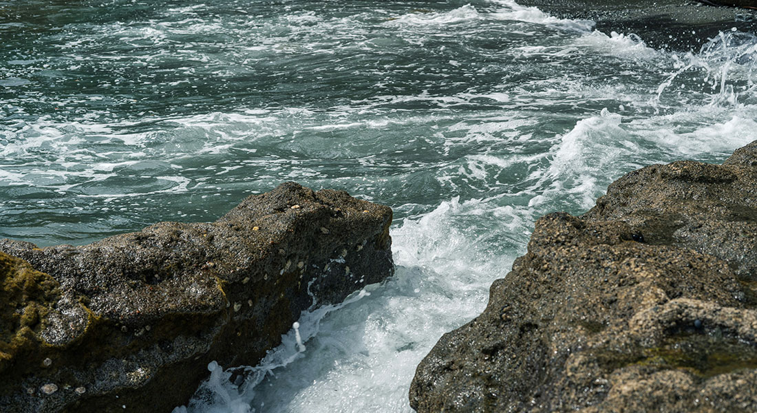 Waves crashing against rocks in the ocean with water splashing and foam visible.