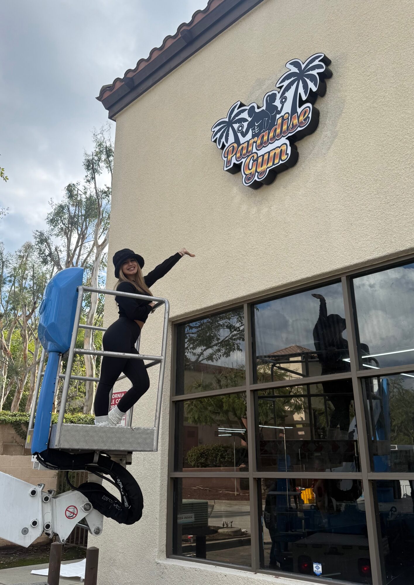 Person standing on a lift outside a building with a sign that says 'Welcome to the Beach'.