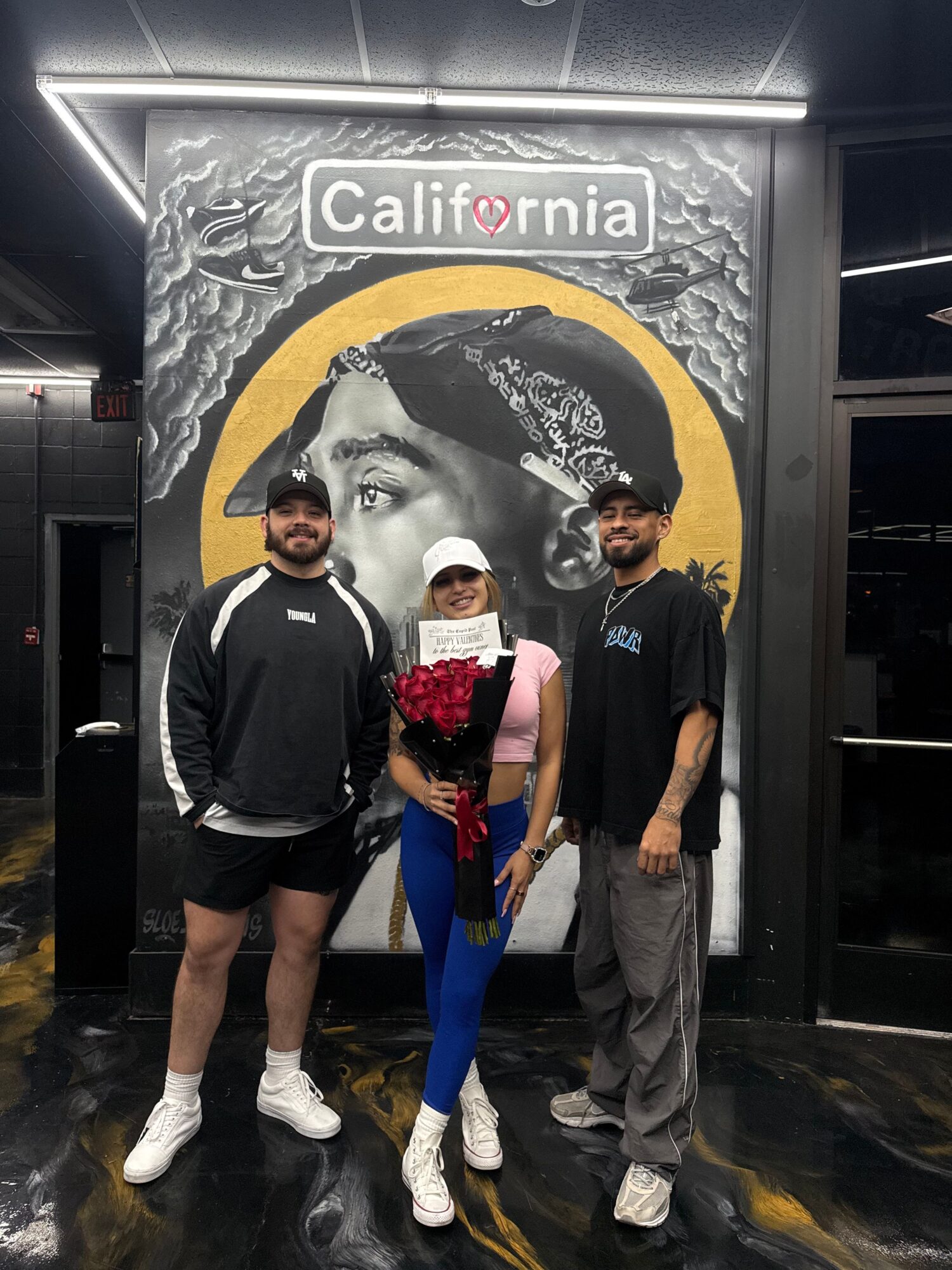 Three people standing in front of a California-themed mural with a woman's face and a yellow circle background.